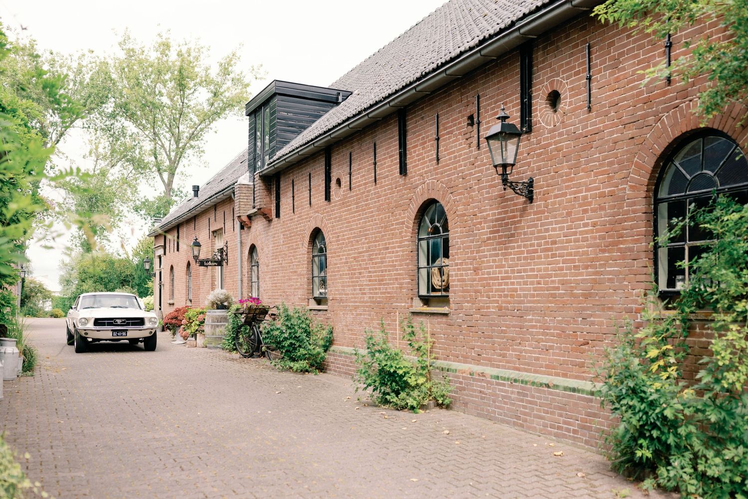 Historic red brick building with arched windows and green foliage along a curved pathway.