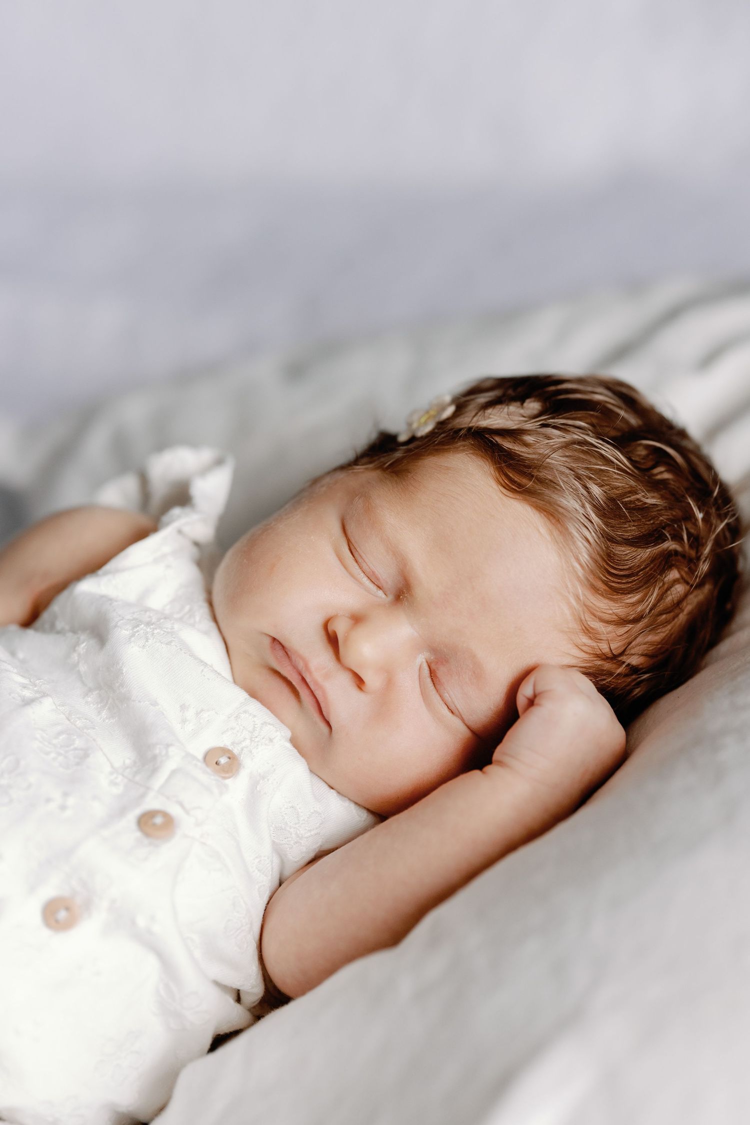 A sleeping infant in white clothing rests on soft white bedding.