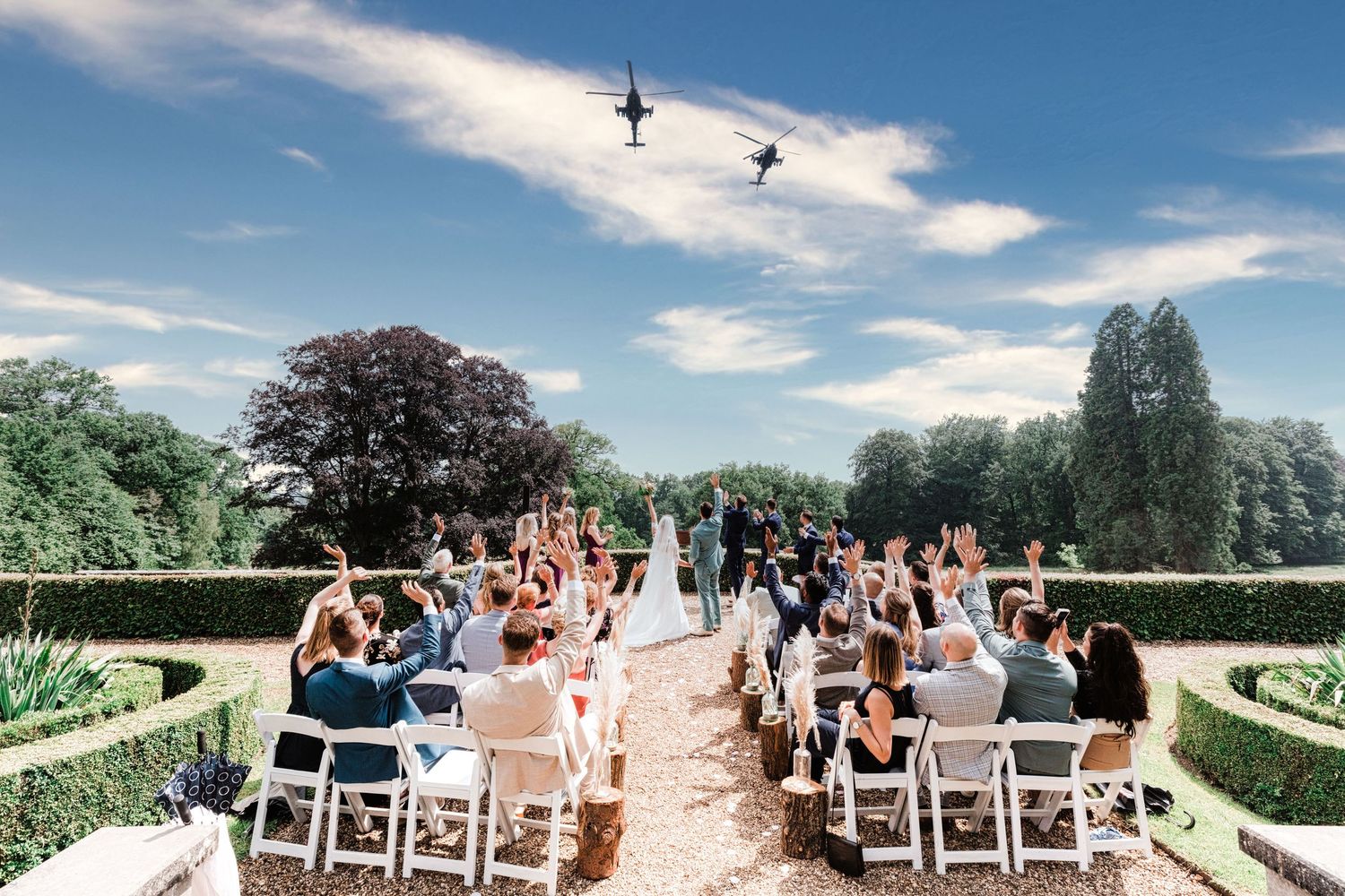 Outdoor wedding ceremony setup with white chairs on a garden path as military jets fly overhead in the blue sky.