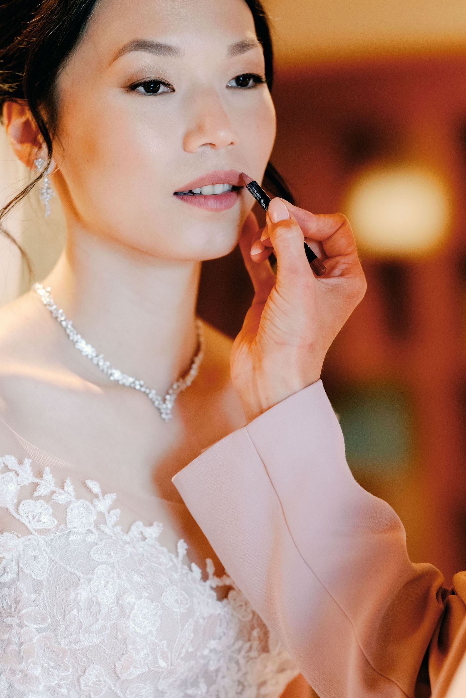 Close-up shots of a bride getting her makeup done while wearing a sparkling necklace and white lace dress.