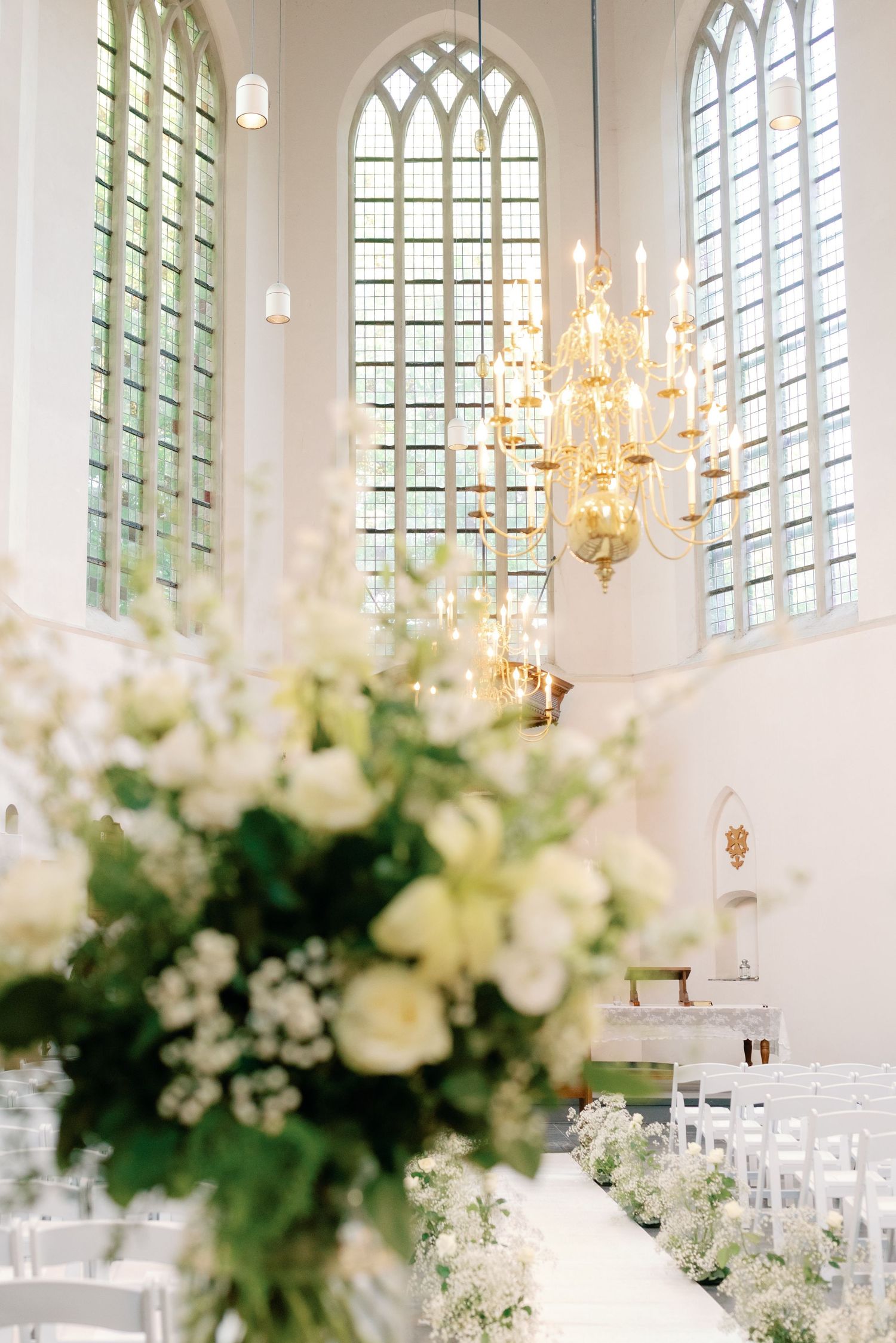 Elegant church interior with Gothic windows, crystal chandeliers and white floral arrangements for a wedding ceremony.