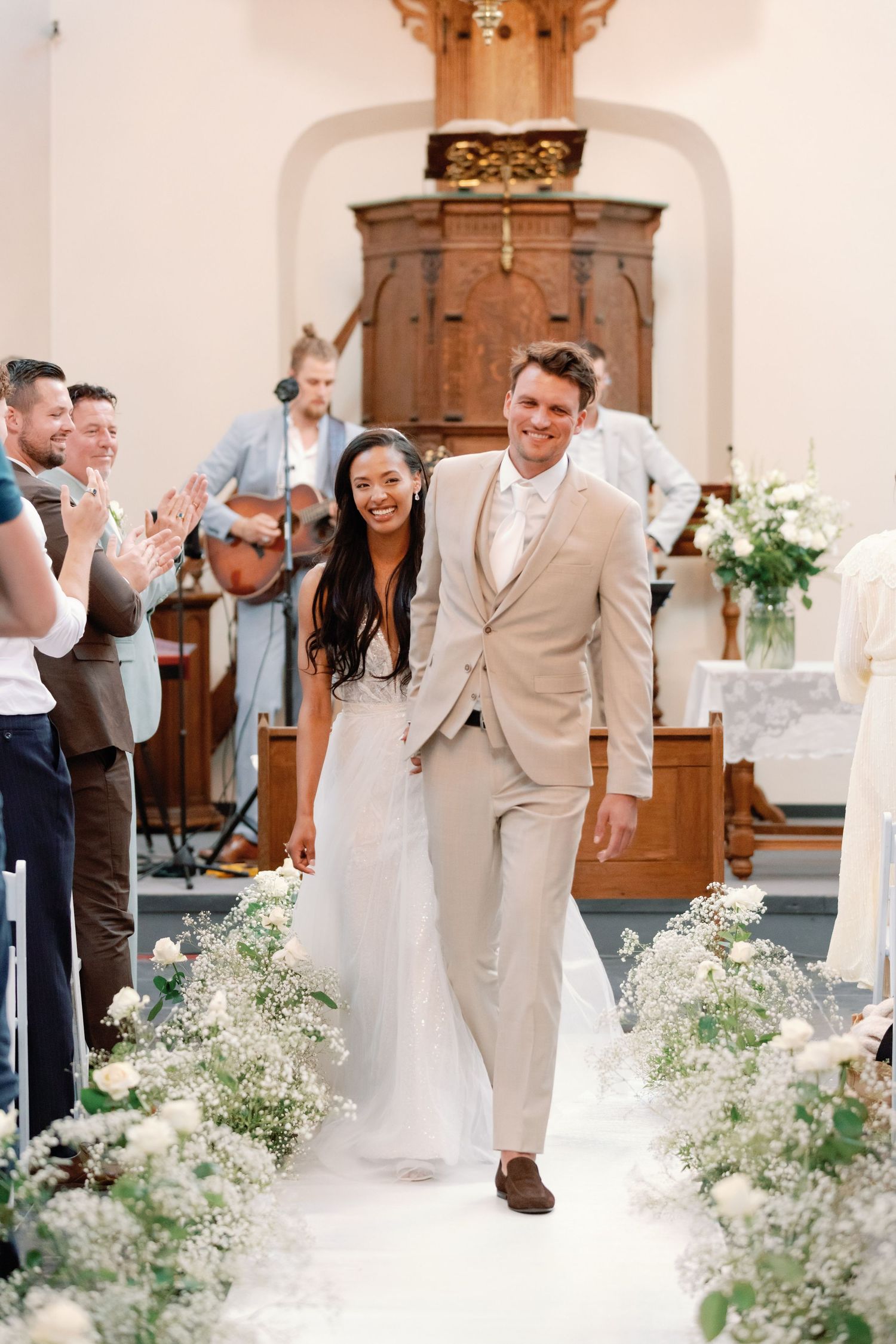 Wedding ceremony aisle decorated with delicate baby's breath flowers and white petals in a bright church setting.