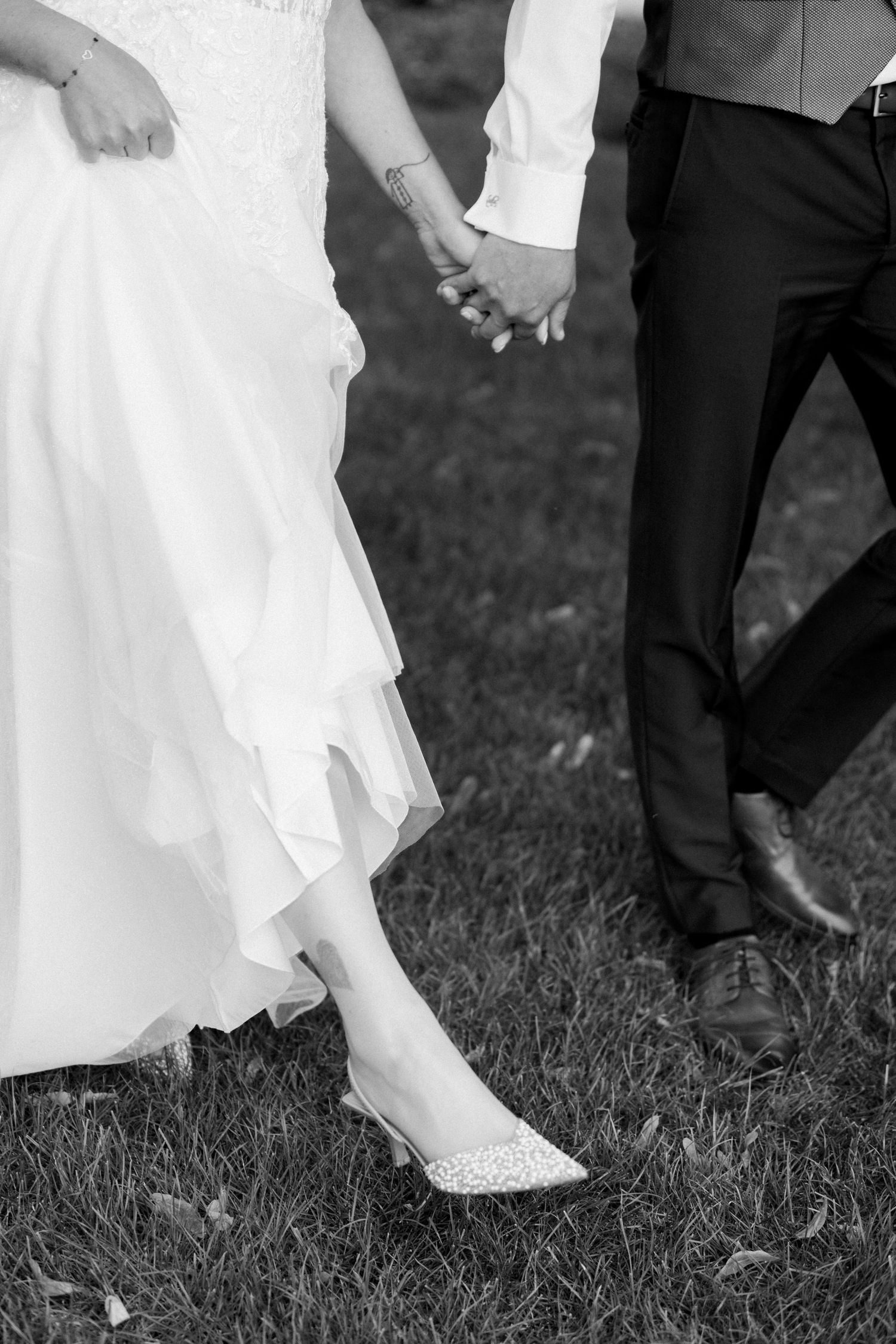 Black and white detail shot of wedding shoes and dress hem on grass.