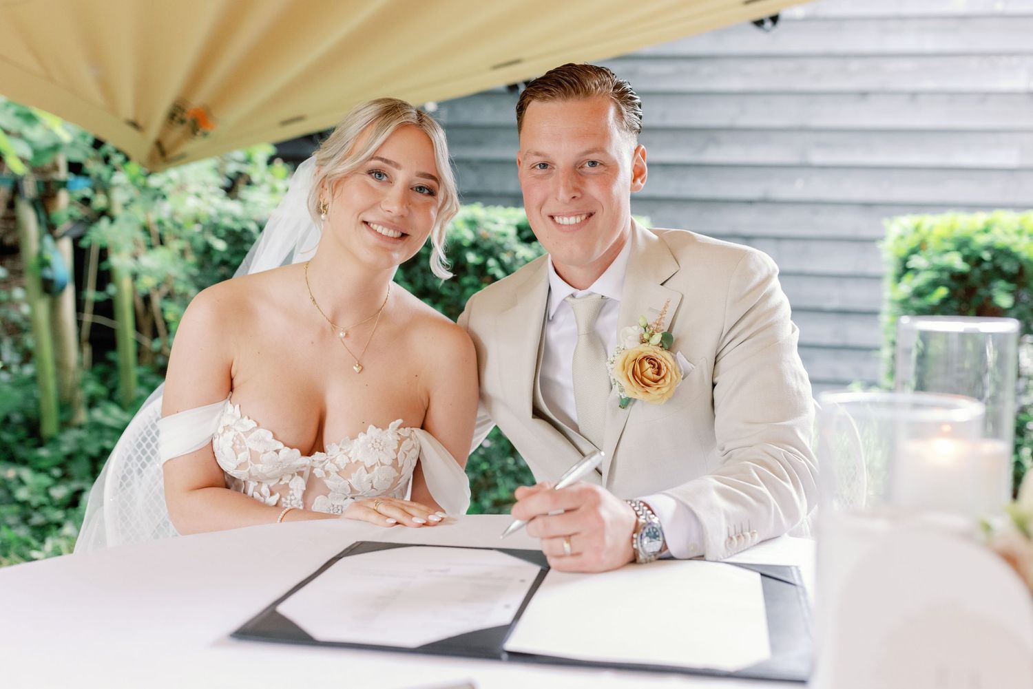 A couple signs their marriage license together at a white gazebo during an outdoor wedding ceremony.