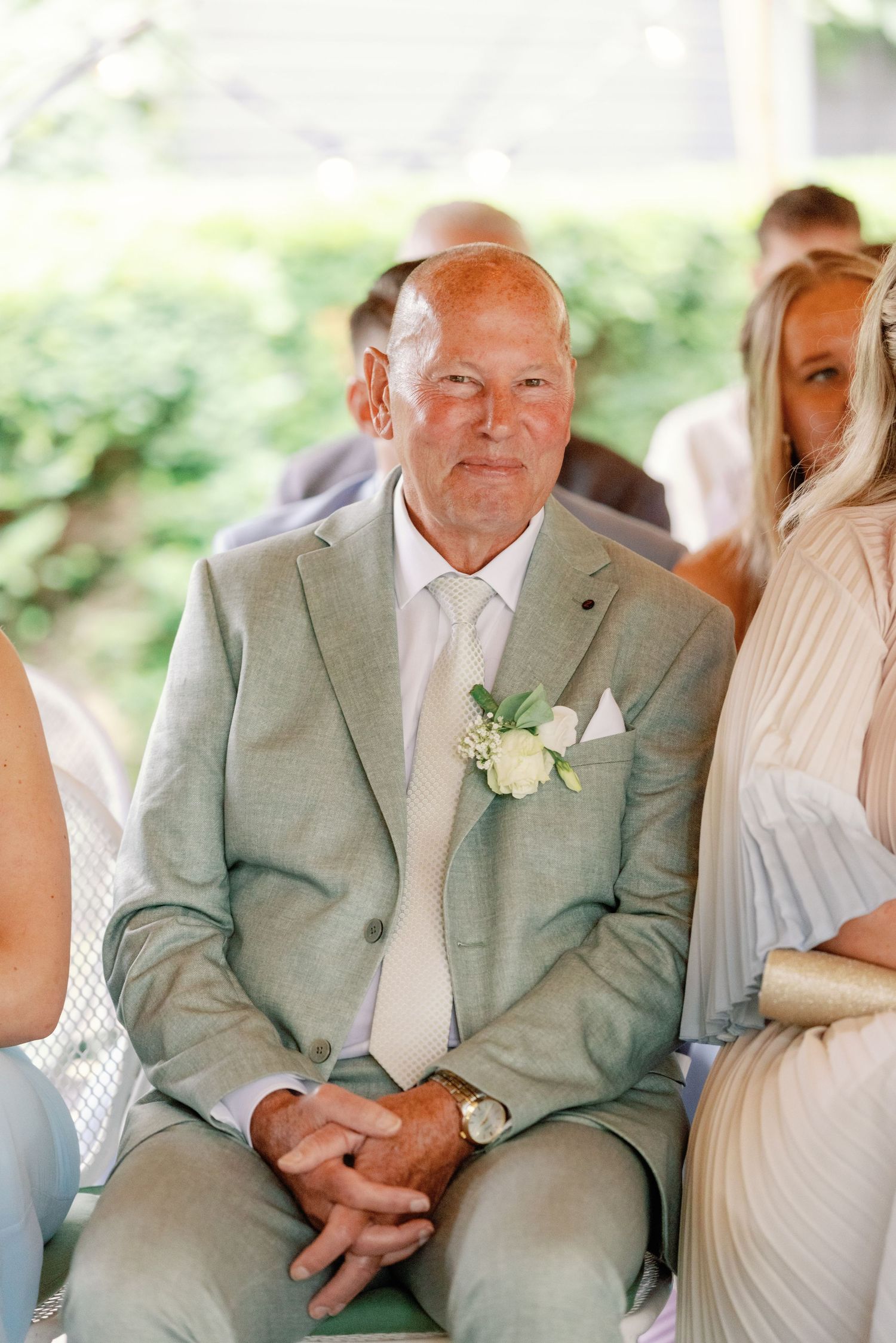 A series of four candid wedding photos showing an older gentleman in a light gray suit sitting at an outdoor event.