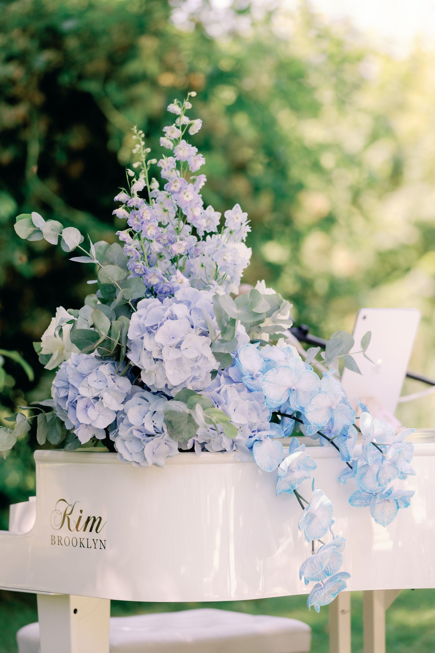 Blue hydrangea and delphinium wedding floral arrangement on white chair with Kim Brooklyn name sign.