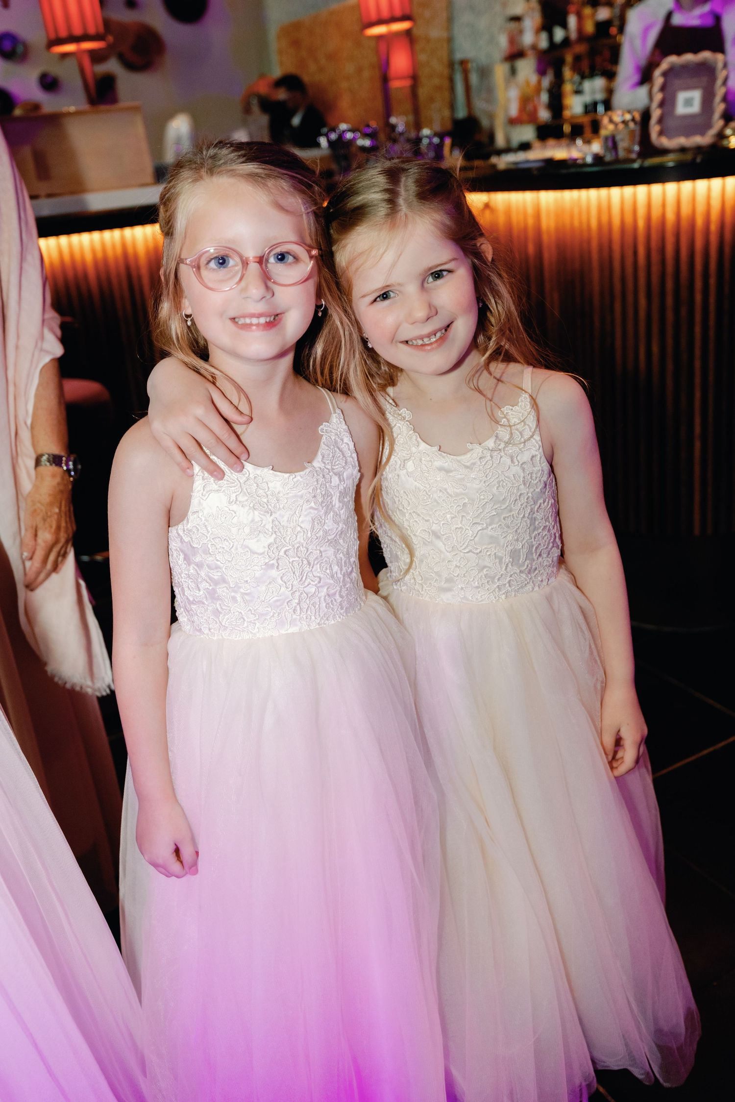 Young flower girls in matching white and pink ombre tulle dresses pose together at a formal event.