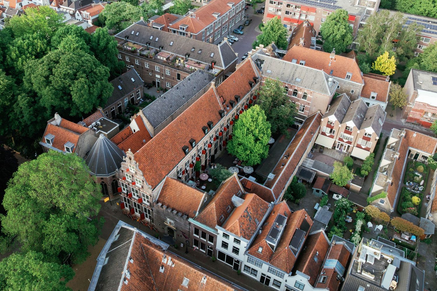 Aerial view of European city rooftops with traditional orange terracotta tiles and green trees surrounding buildings.