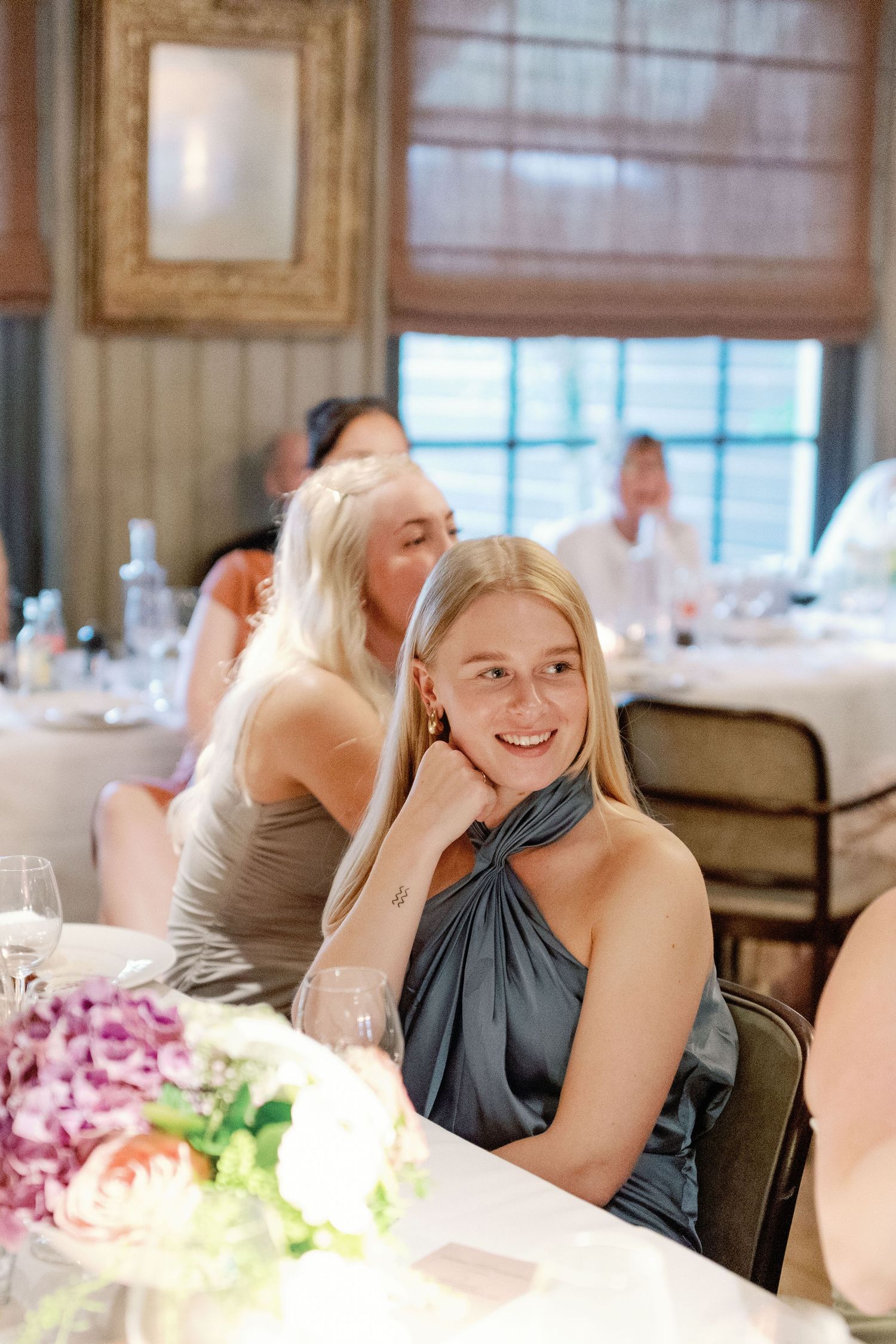 Guests enjoy an elegant dinner party with floral centerpieces and formal table settings in an indoor venue.