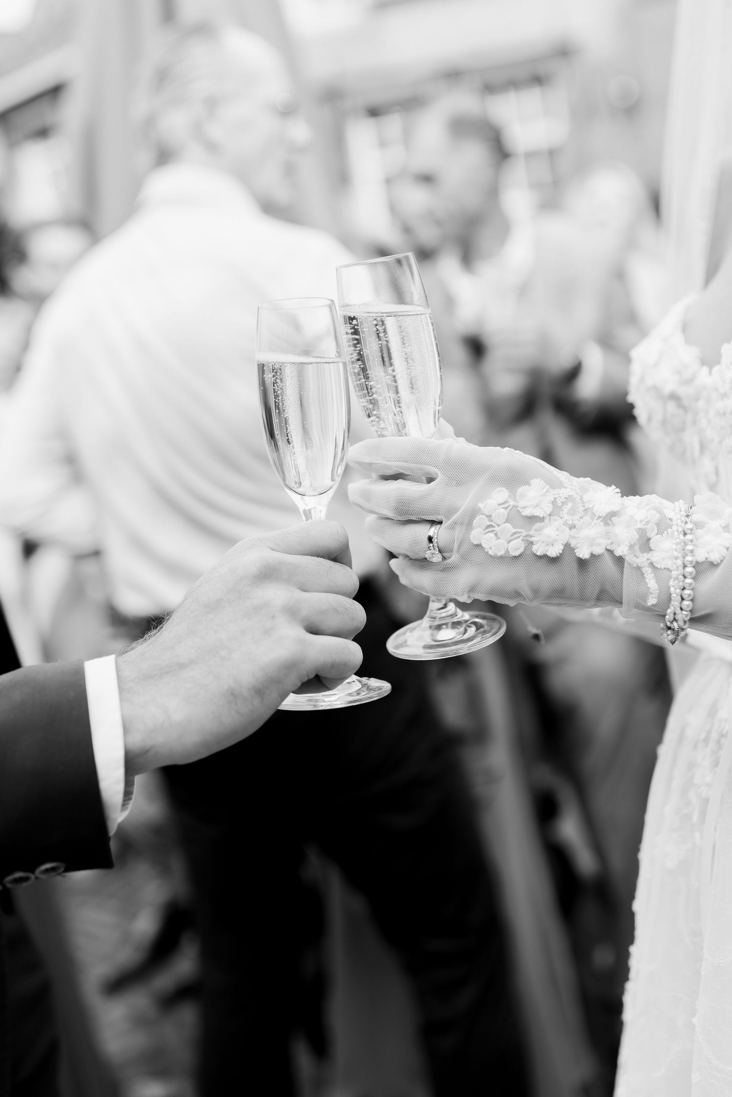 Black and white photo of champagne glasses clinking in a toast at a wedding celebration.