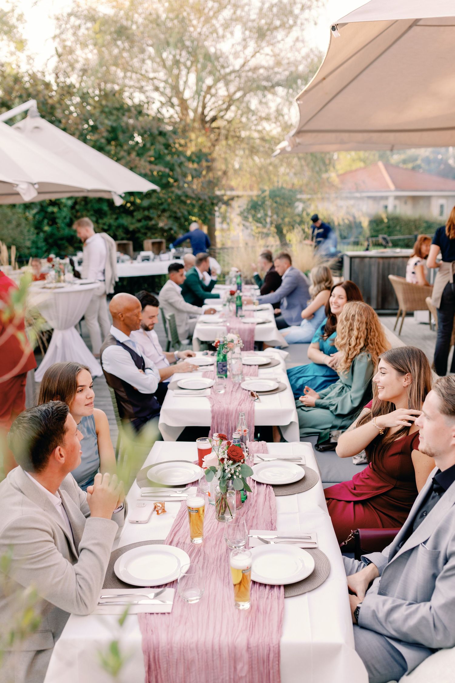 Long dining table set with pink linens and place settings for an outdoor wedding reception.