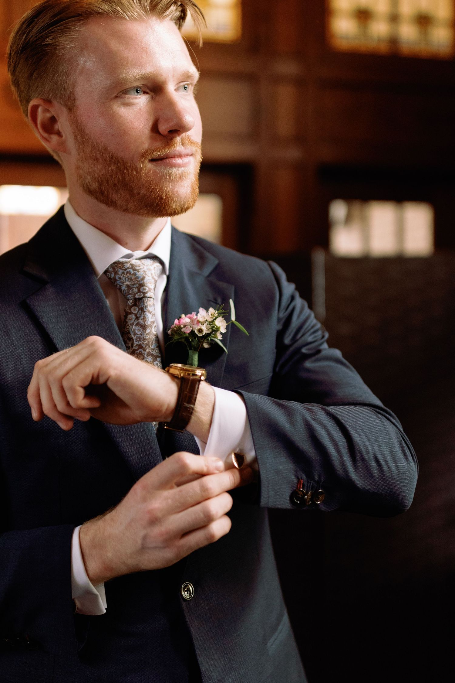 A groom in a dark suit adjusts his tie while getting ready for a formal event.