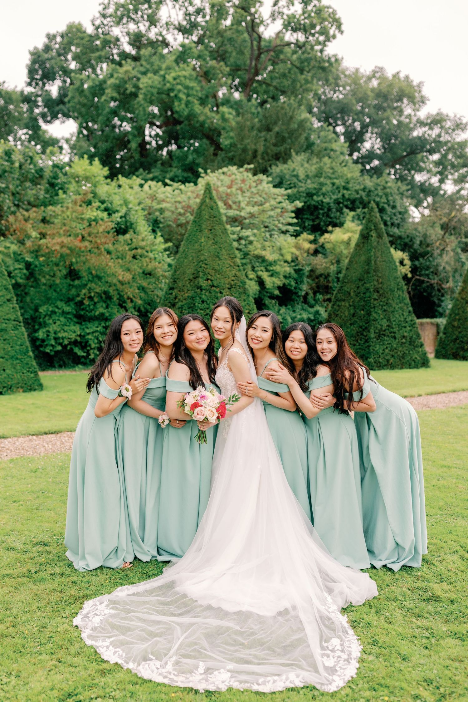 Bridesmaids in mint green dresses pose with bride on lush garden lawn.