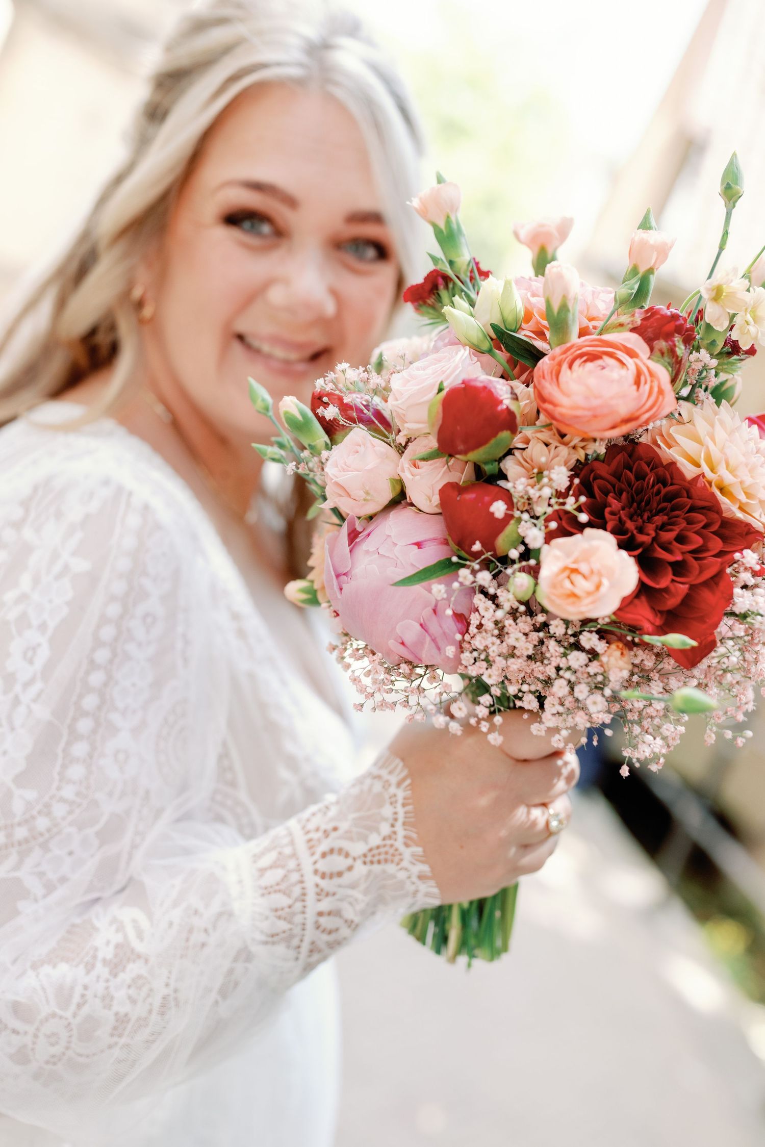 A bridal portrait series showing close-up details of lace sleeves and a romantic coral and burgundy floral bouquet.