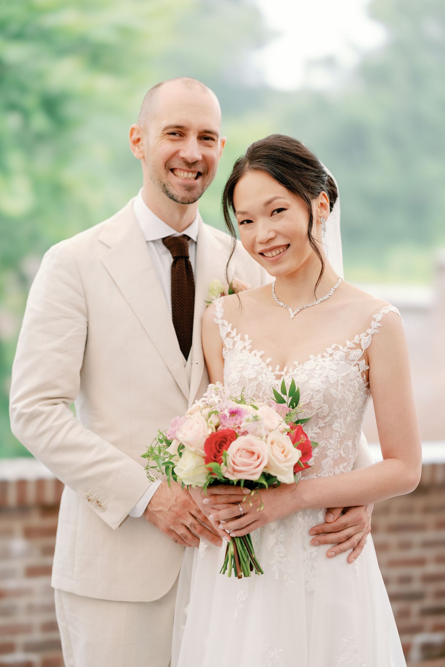 A happy couple shares joyful moments on their wedding day in a garden setting with pink floral bouquet.