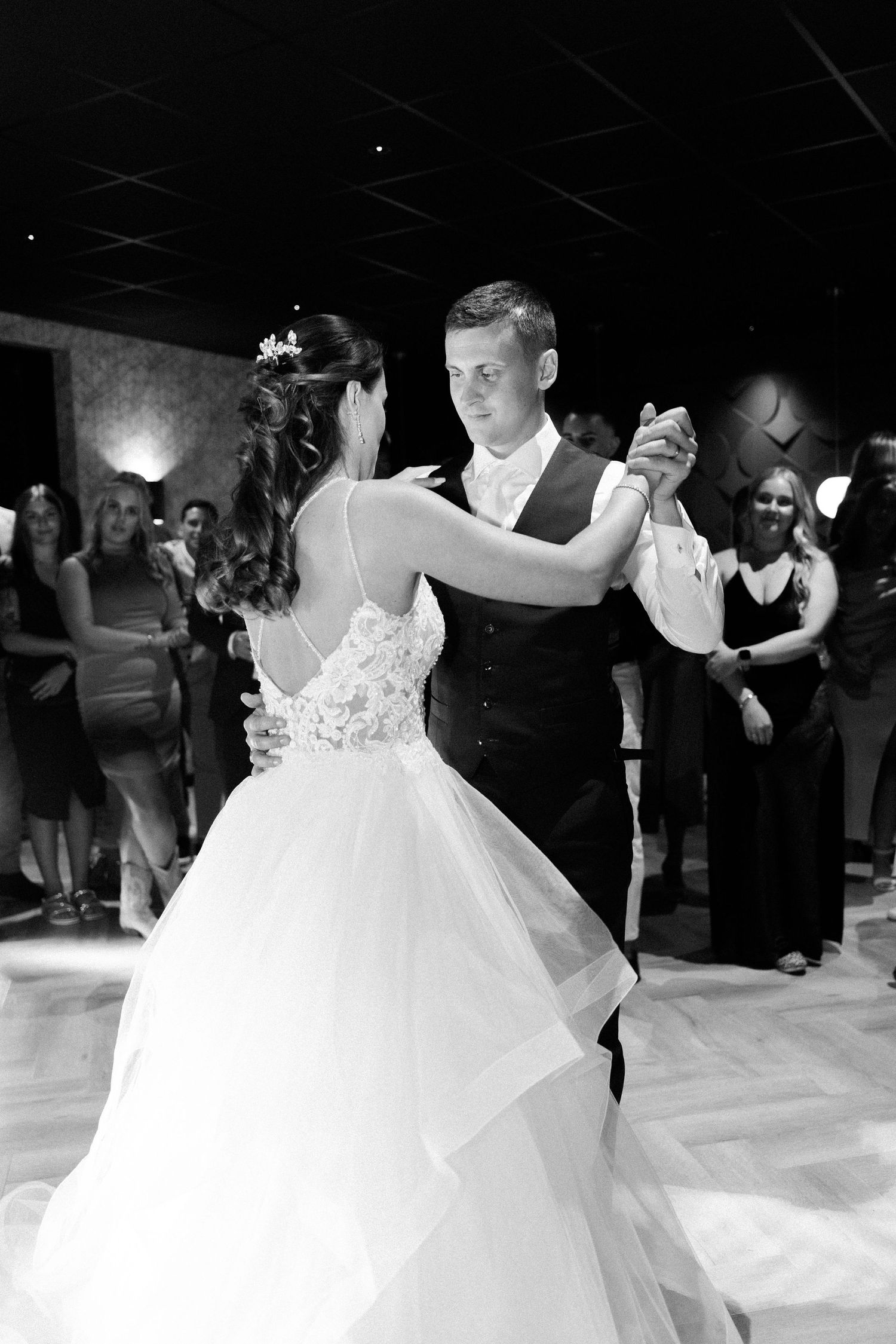 A couple performs an elegant dance on a wooden floor during their wedding reception.