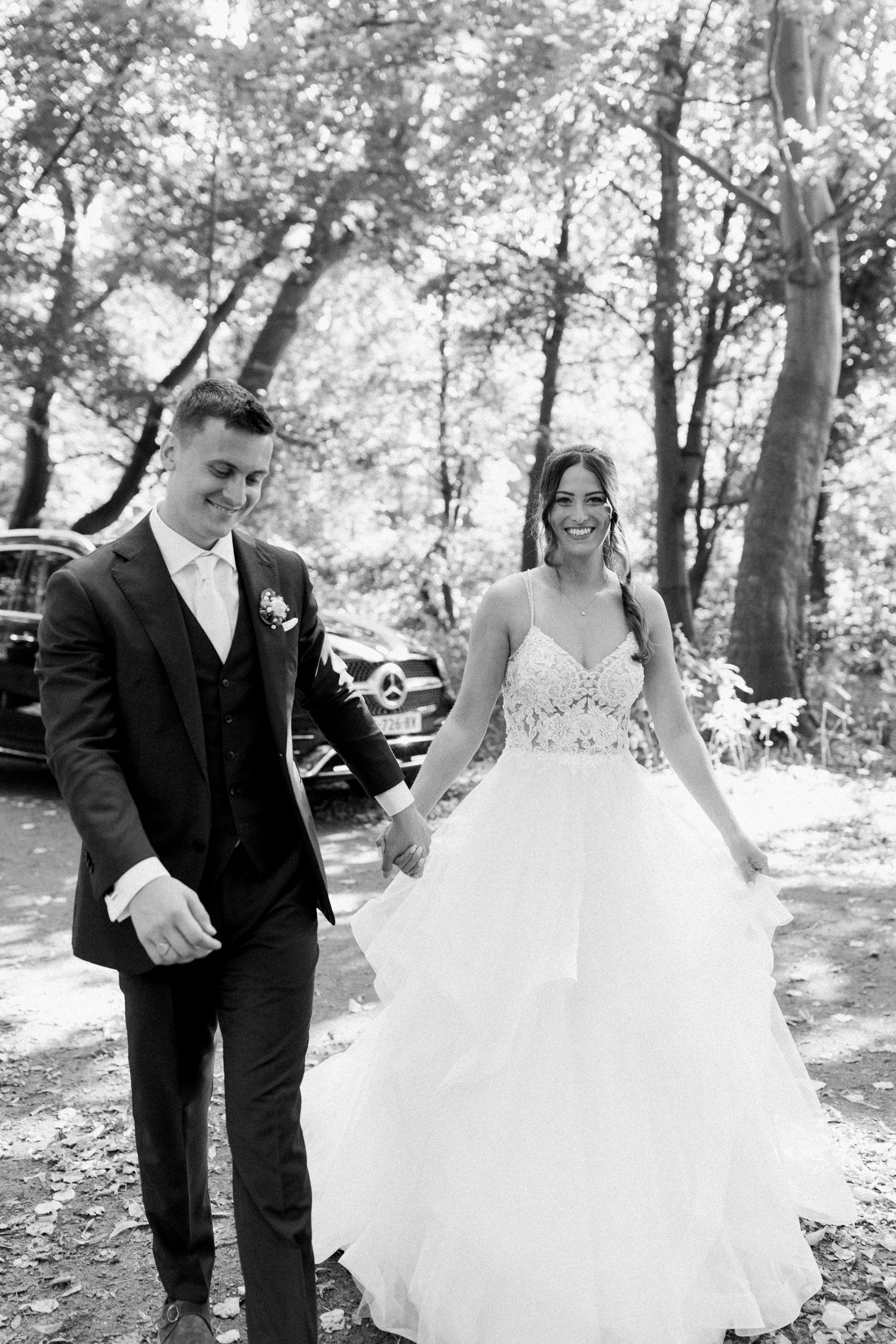 A black and white portrait of newlyweds walking together in a forest setting.