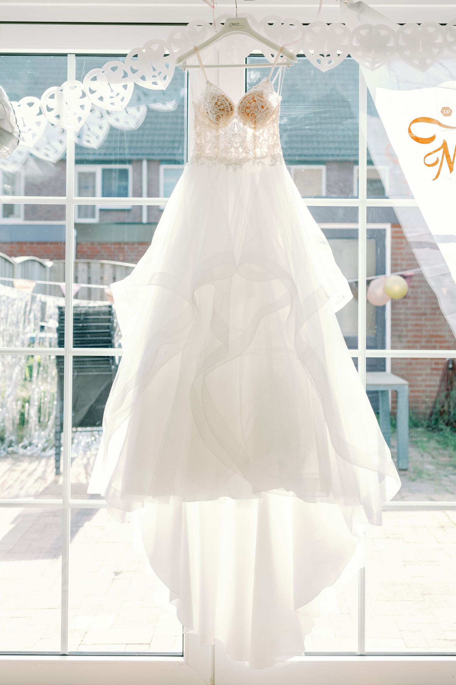 Ethereal white wedding dress hangs by sunlit windows creating a dreamy silhouette.