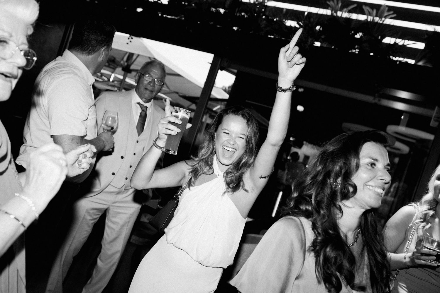 A black and white photo shows people dancing and celebrating at what appears to be a lively party or reception.