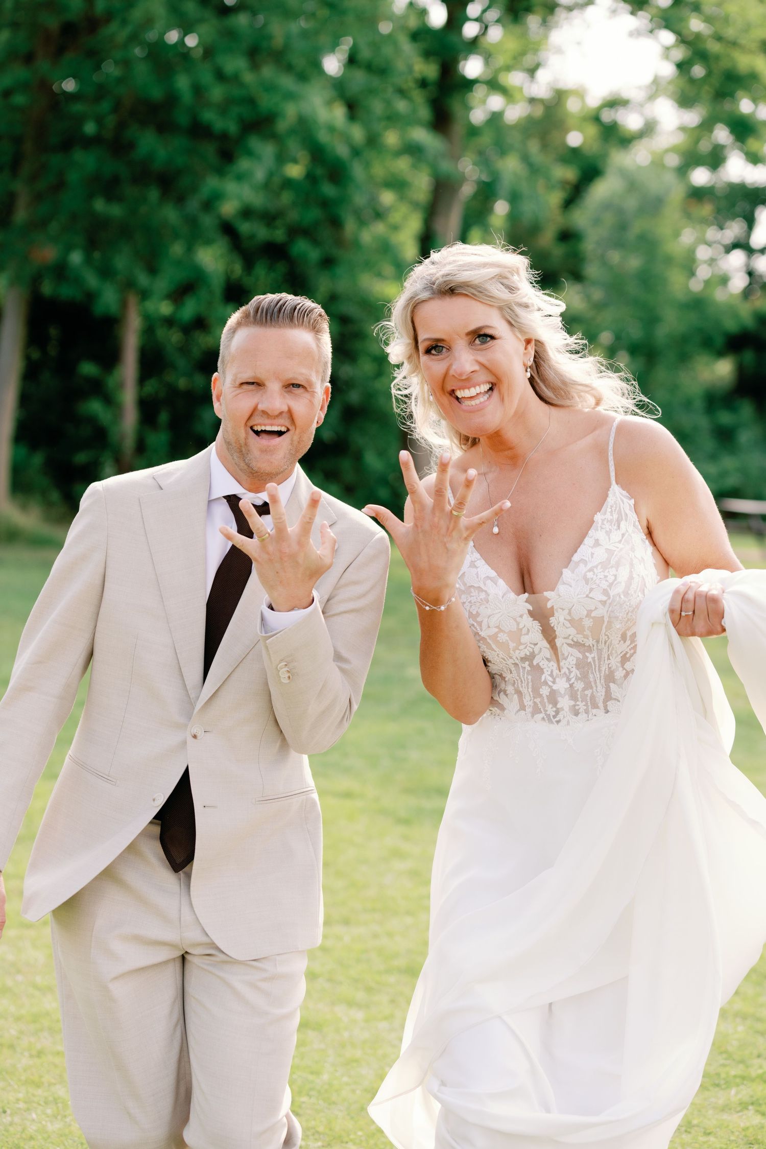 A couple in wedding attire share joyful candid moments while posing together outdoors on a sunny day.