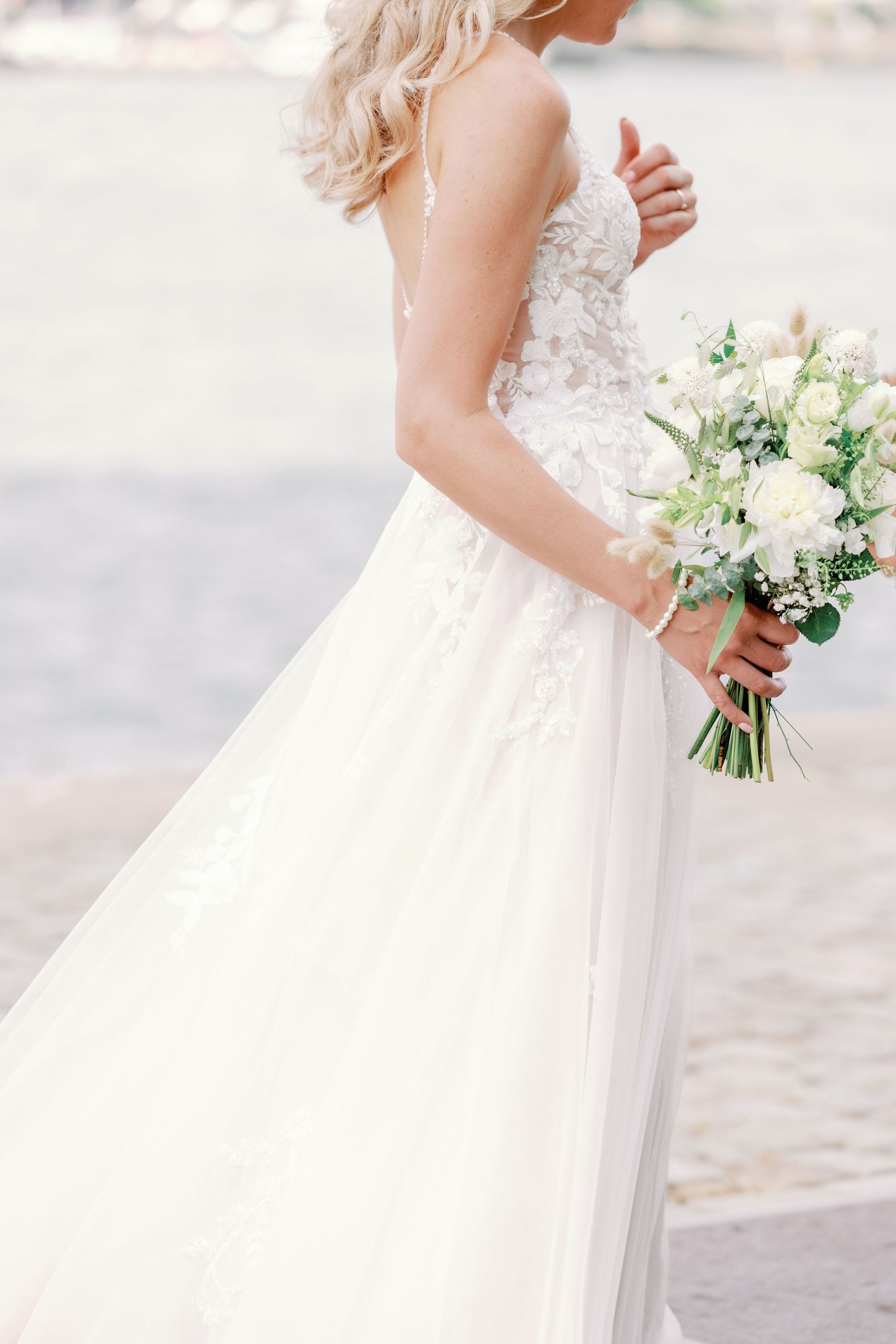 A romantic wedding dress detail showing delicate lace bodice and flowing tulle skirt with white floral bouquet.