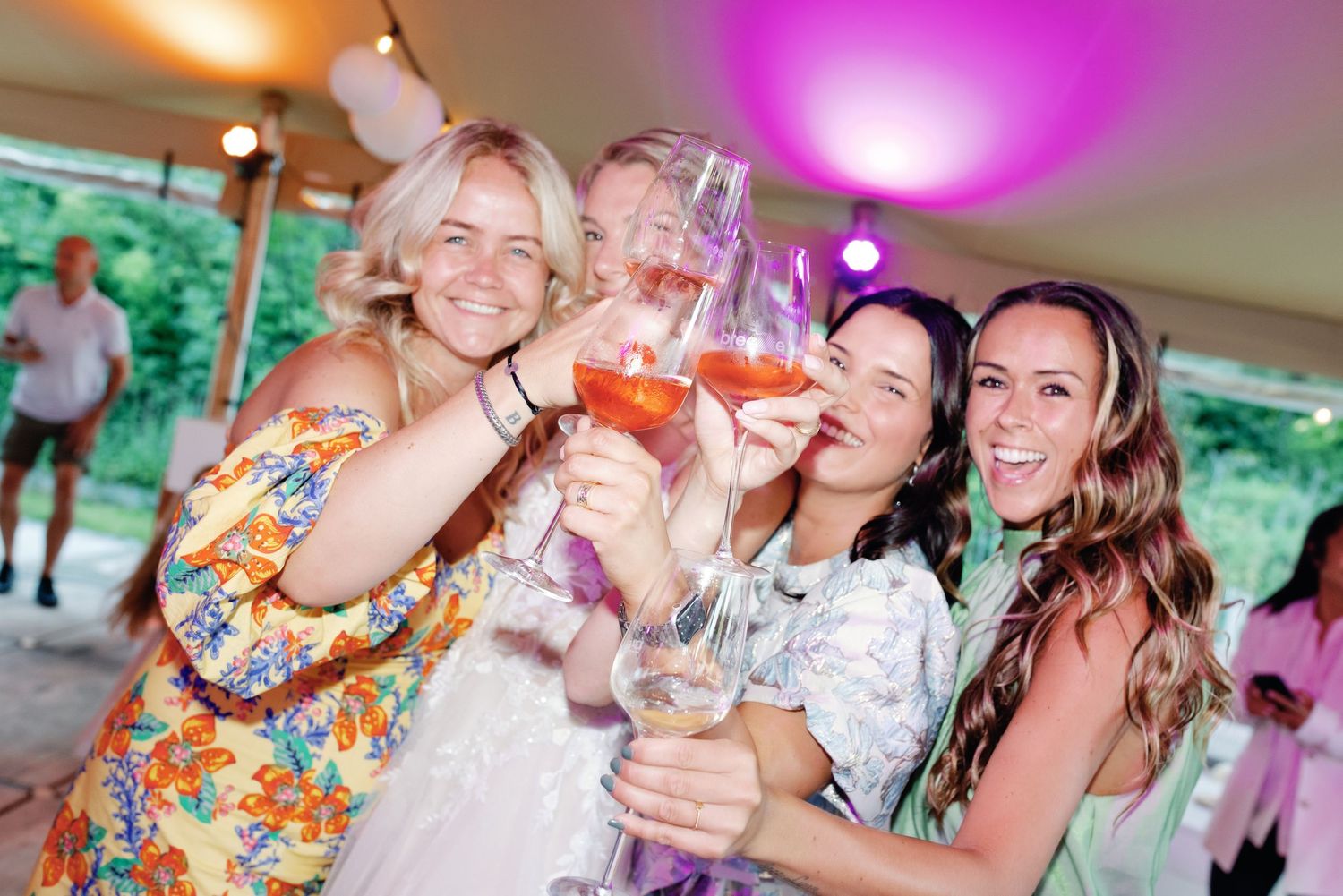 A group of people celebrating at a party with colorful lighting and raised glasses.