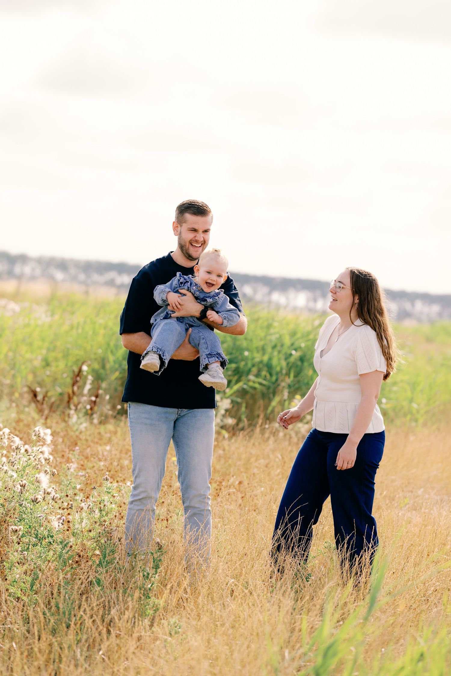 A happy young family with a baby enjoying a sunny day in a golden meadow field outdoors.