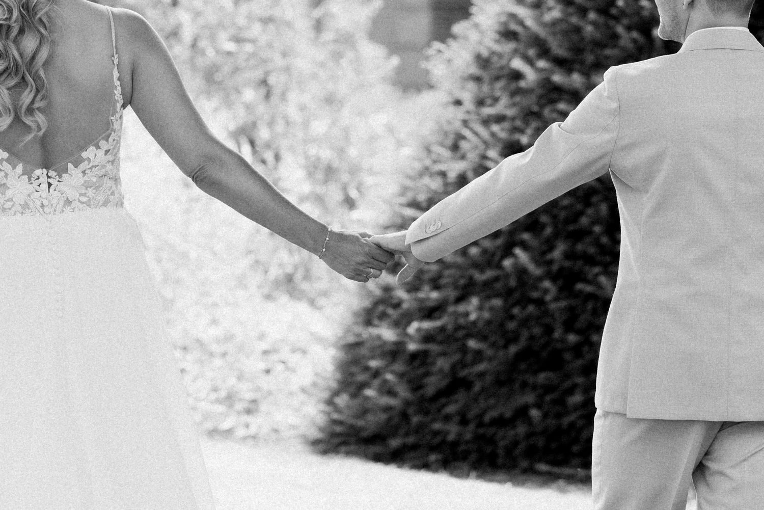A couple in wedding attire dances together outdoors surrounded by nature and greenery.
