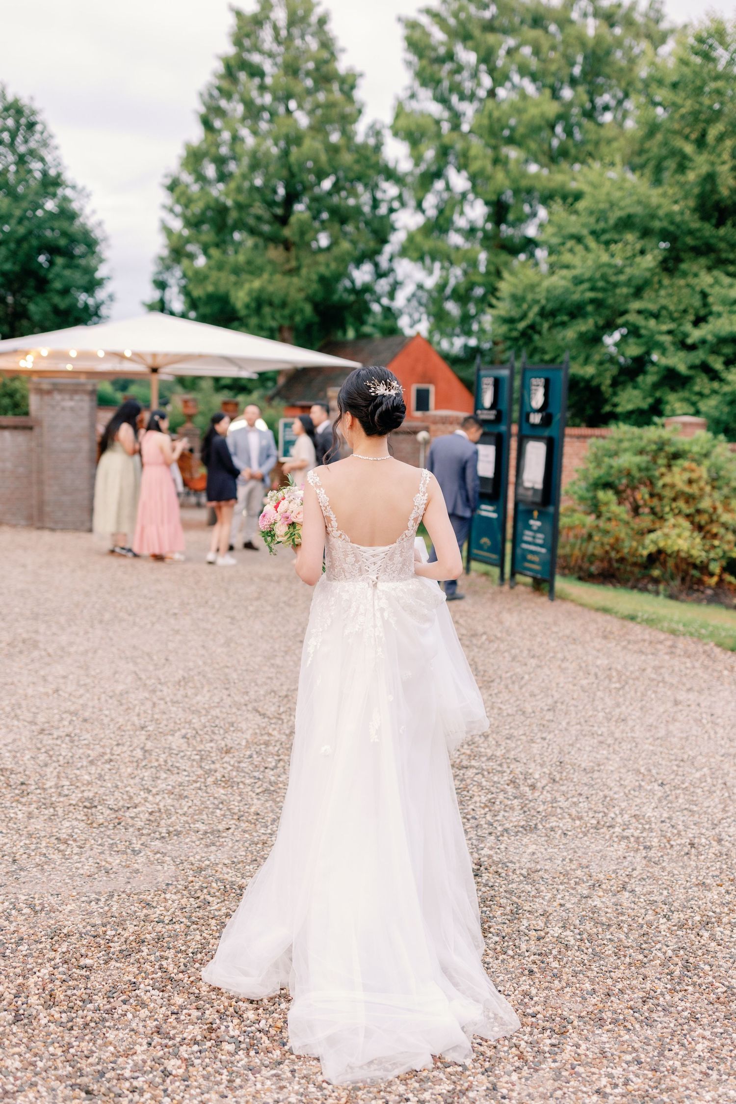Wedding party walking on gravel path in elegant dresses and gowns at outdoor venue.