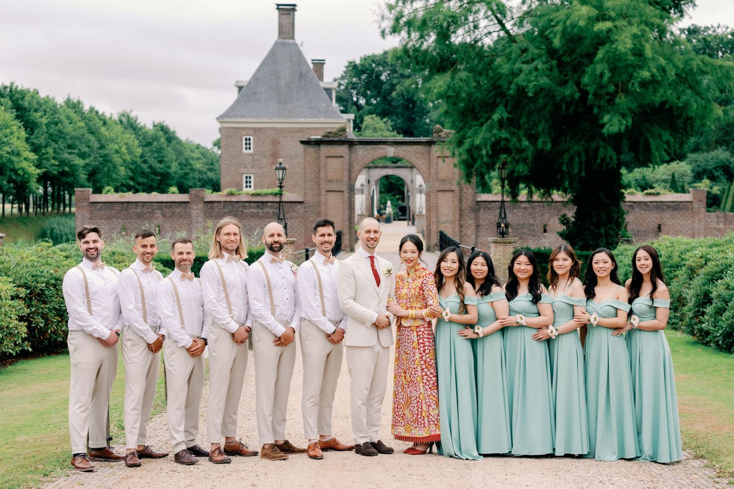 Wedding party members in coordinated mint green dresses and beige suits pose outdoors near historic buildings.