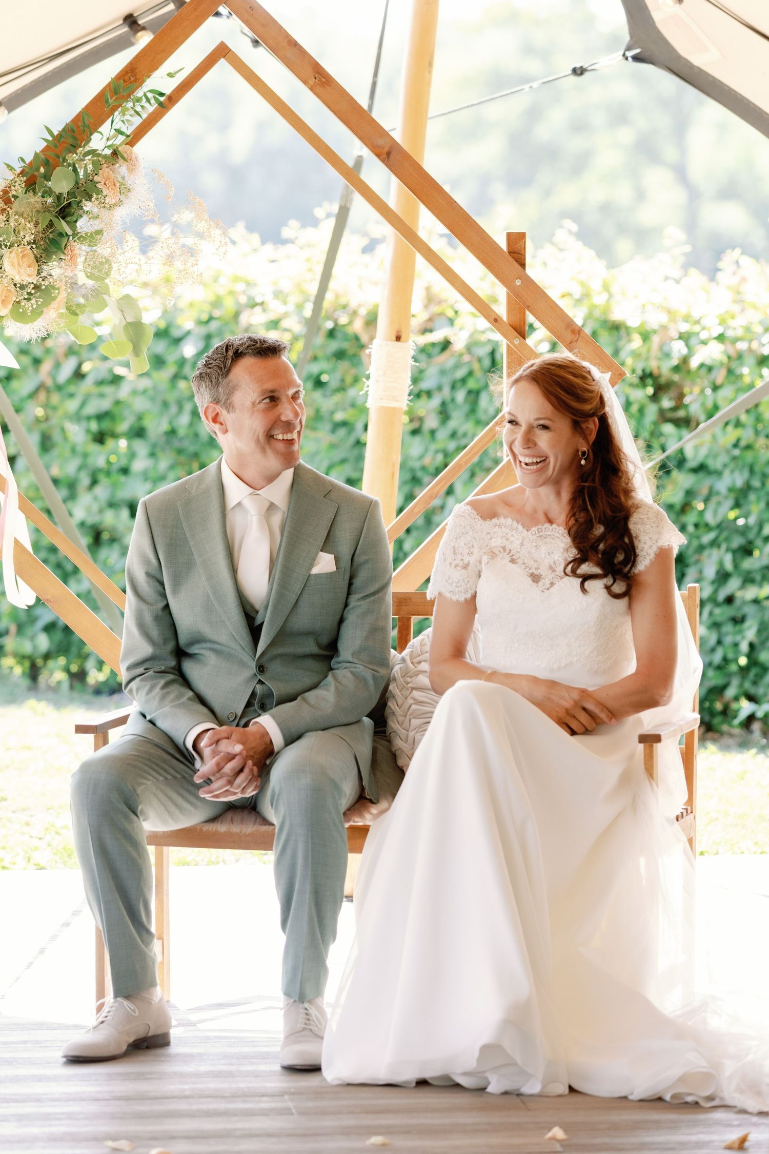 A couple in wedding attire sits and shares a candid moment together on a covered porch.