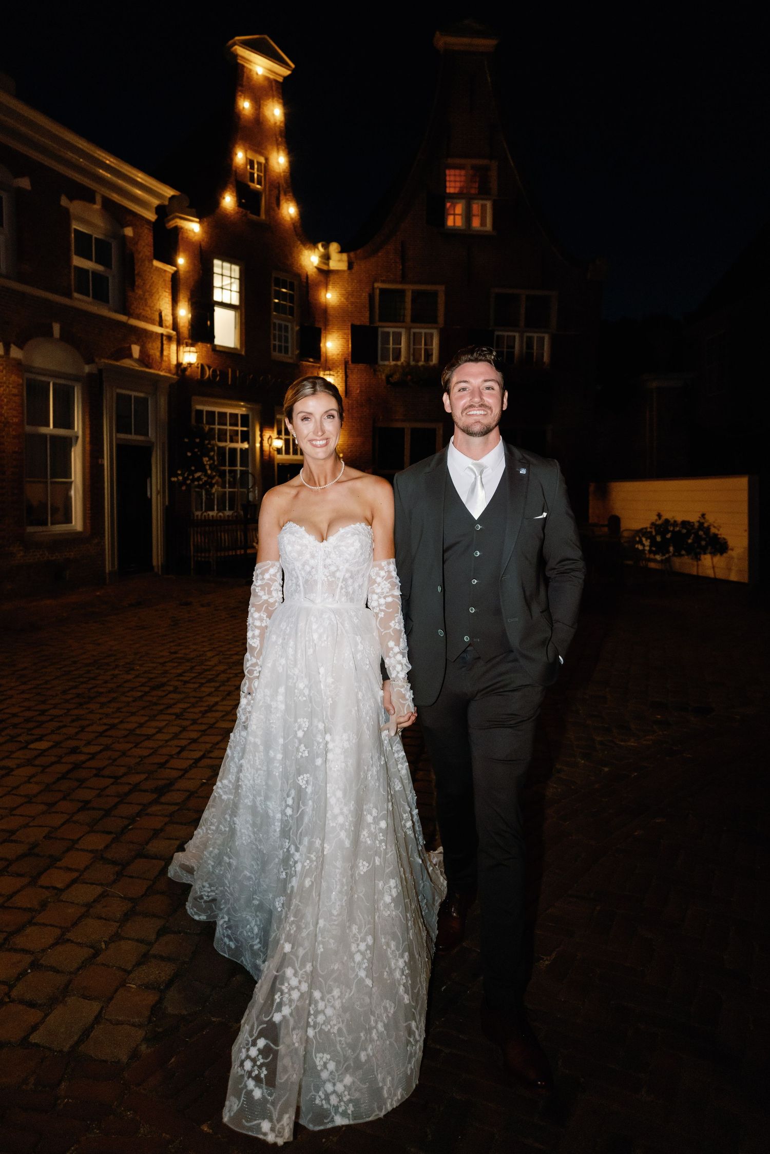 A couple poses at night on cobblestone streets, with the bride wearing a sparkly off-shoulder wedding gown.
