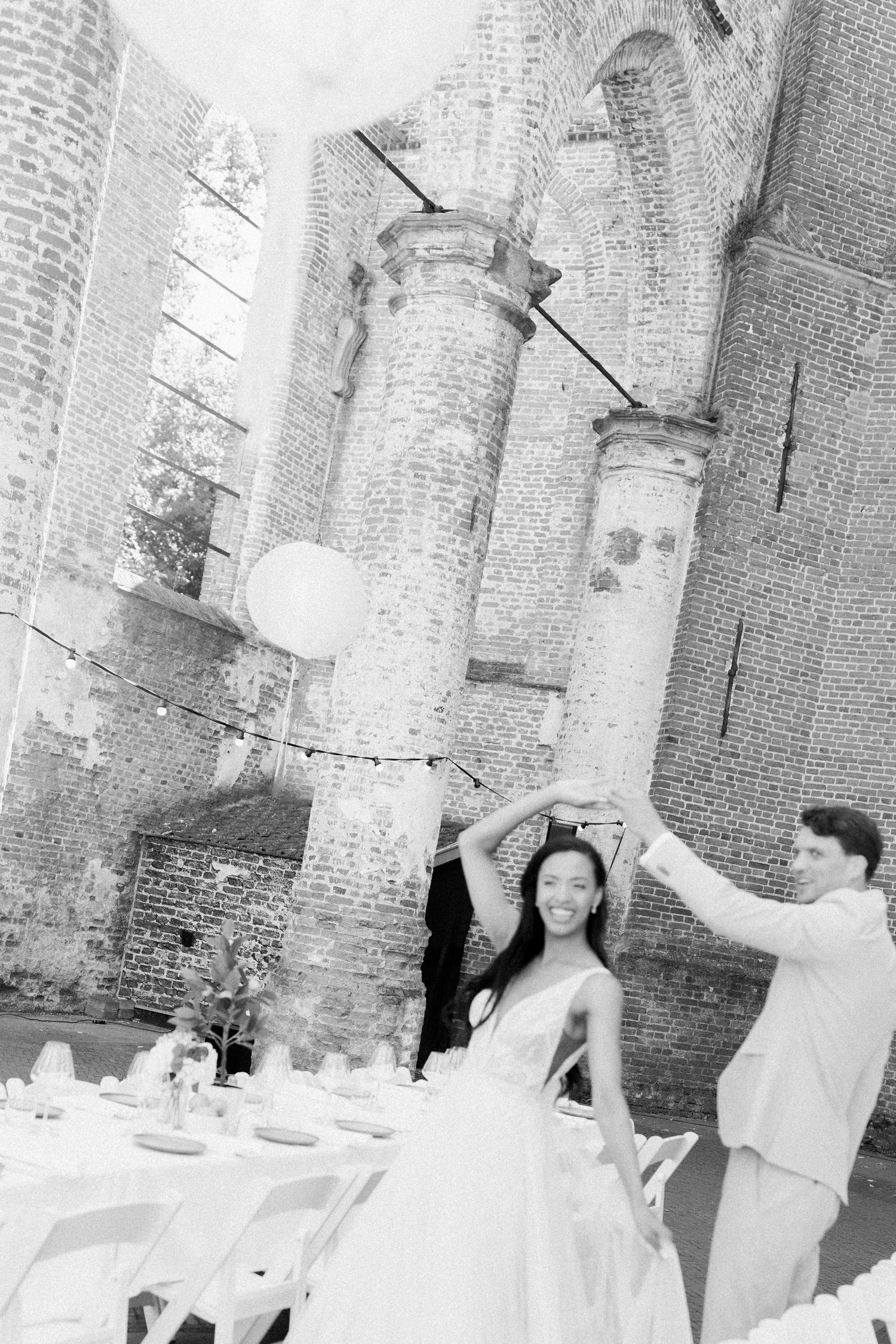 A series of black and white photos showing a dining table setting with white tablecloths in a brick-walled space.