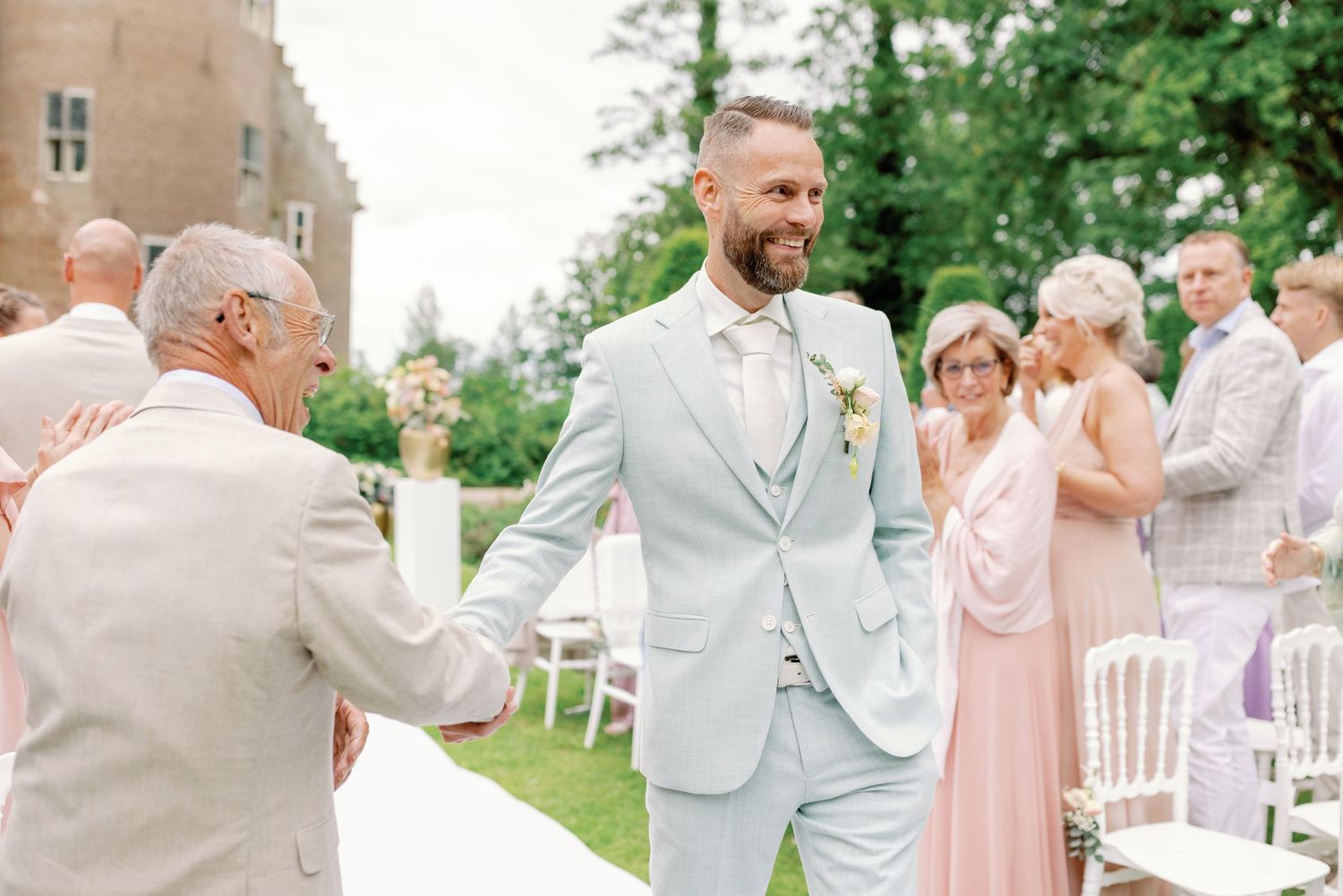 Wedding party members in pastel pink and beige attire celebrate outdoors in a garden setting.