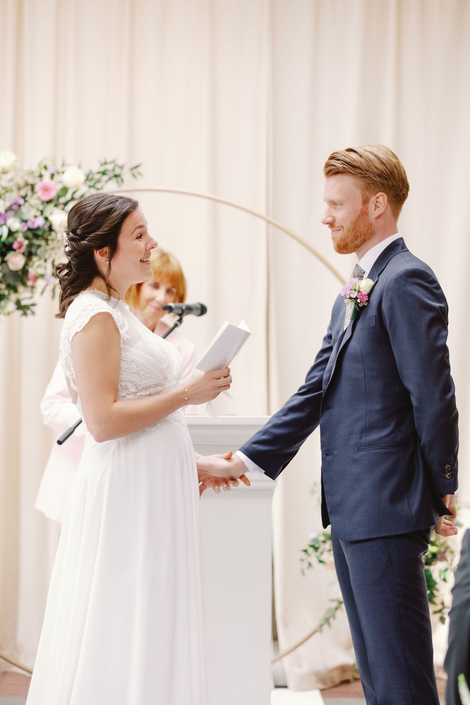 Wedding couple shares a joyful first look moment in an elegant white-columned venue with floral decorations.