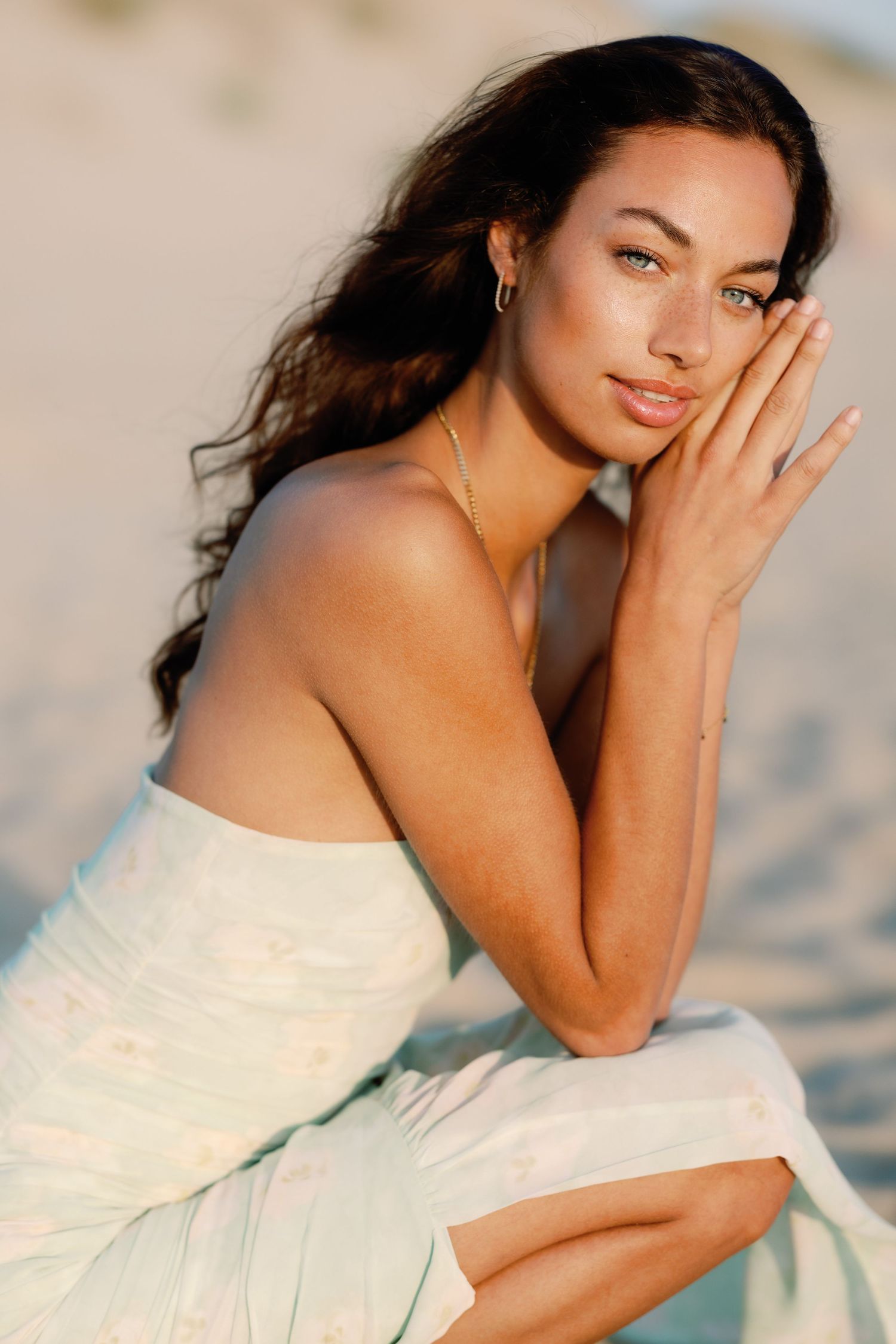 Woman in white dress poses gracefully on beach during sunset photoshoot.