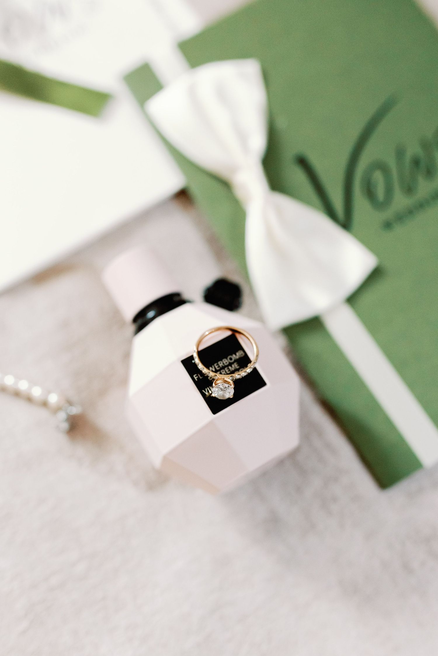 Wedding rings displayed in a pink box with white bow against a green invitation card.