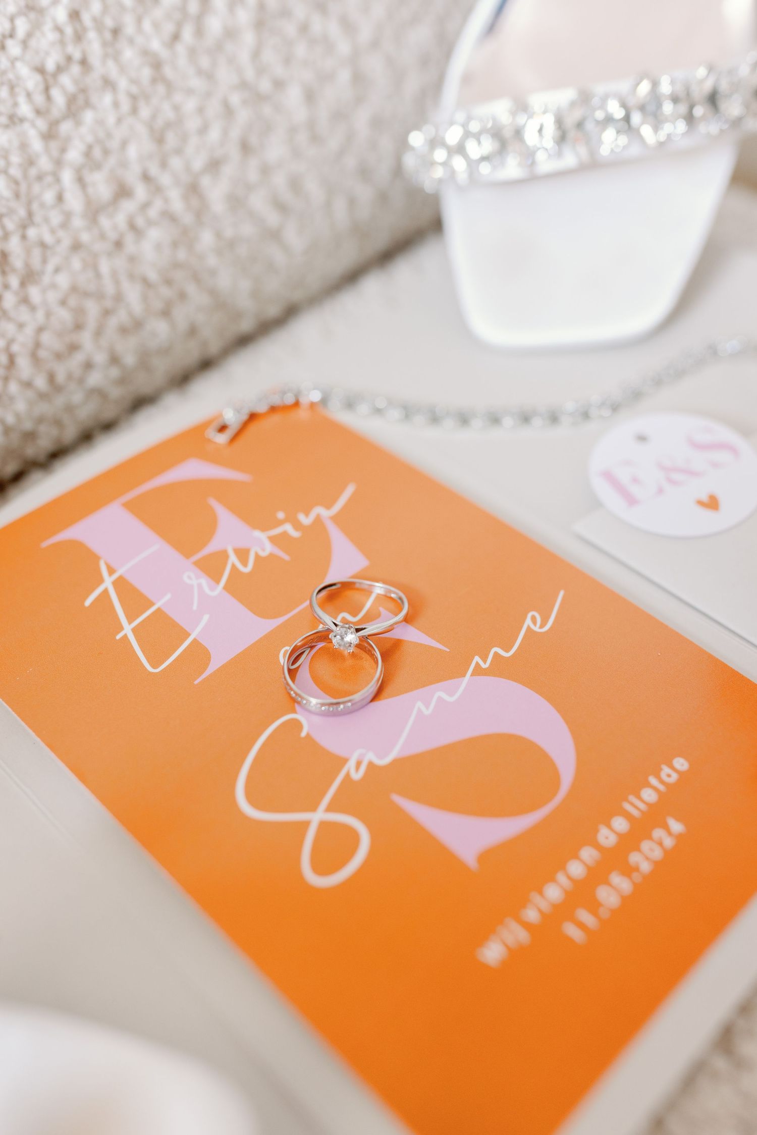 Wedding rings placed on an orange and pink invitation card with elegant typography.
