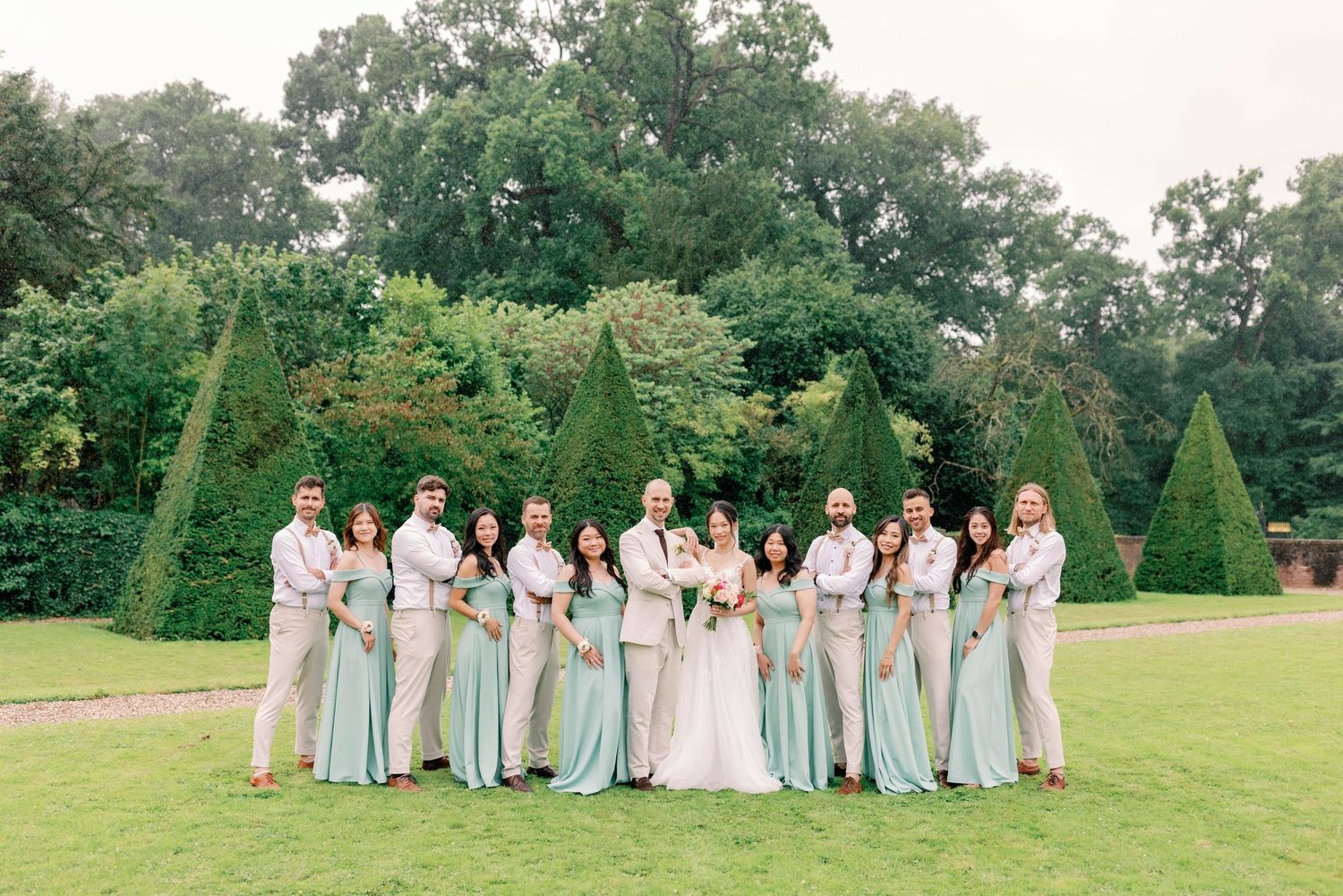 Wedding party in white and cream attire poses on grassy lawn for group photos.