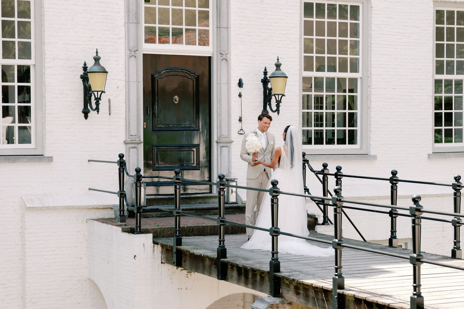 A white colonial-style building entrance with black railings, lanterns, and a person in white standing on the steps.