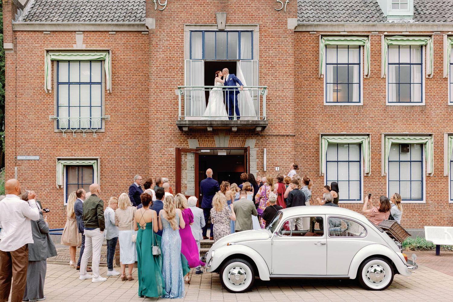 Classic white vintage Volkswagen Beetle decorated as a wedding car parked outside a brick building.