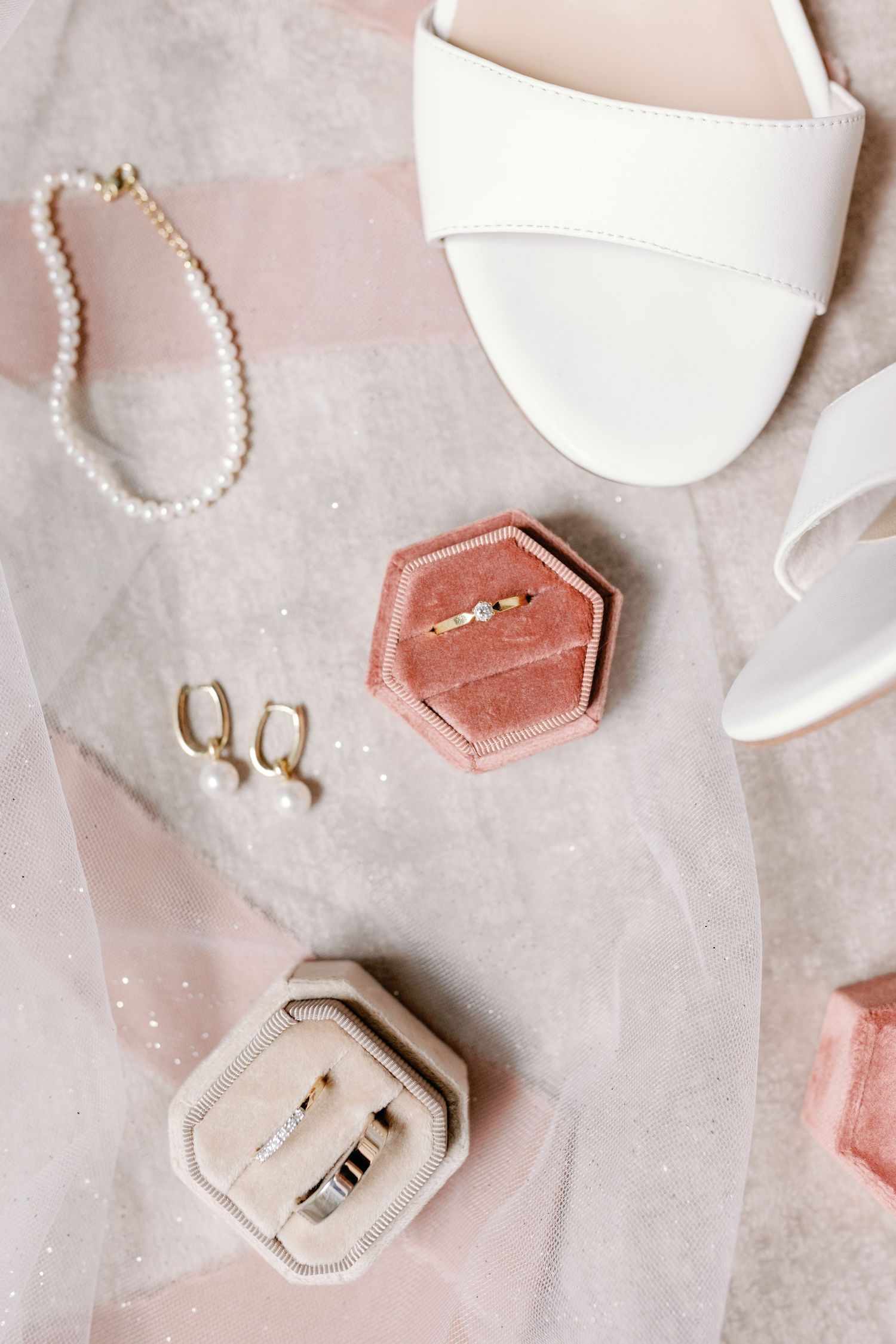 Elegant wedding ring boxes in blush pink and white velvet arranged on a light gray textured surface.