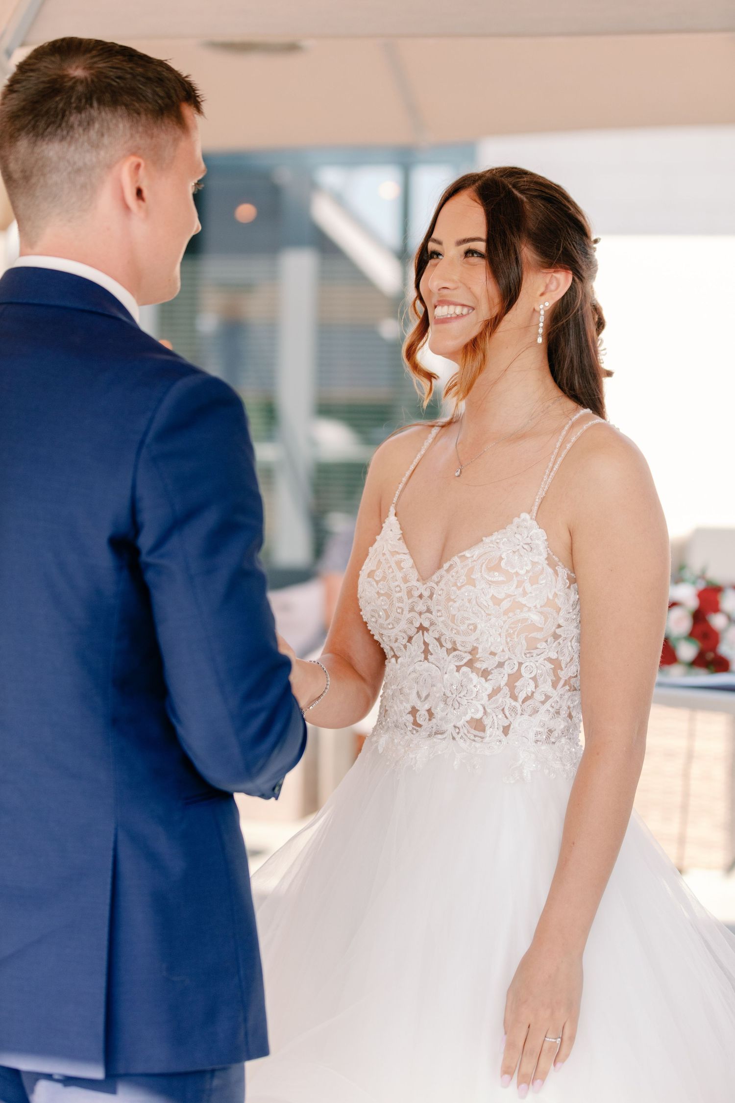 A wedding couple exchanges vows under a covered outdoor venue, with the bride wearing a delicate lace gown.