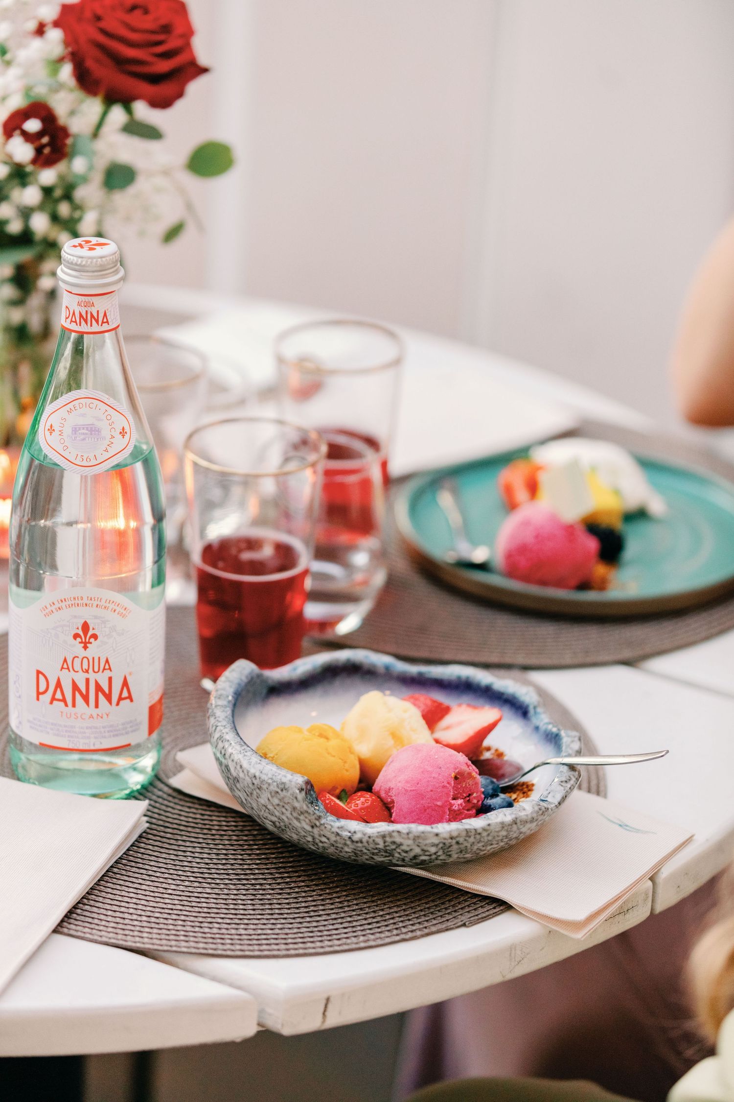 Table setting with Panna water bottles, colorful desserts, and red rose decoration.