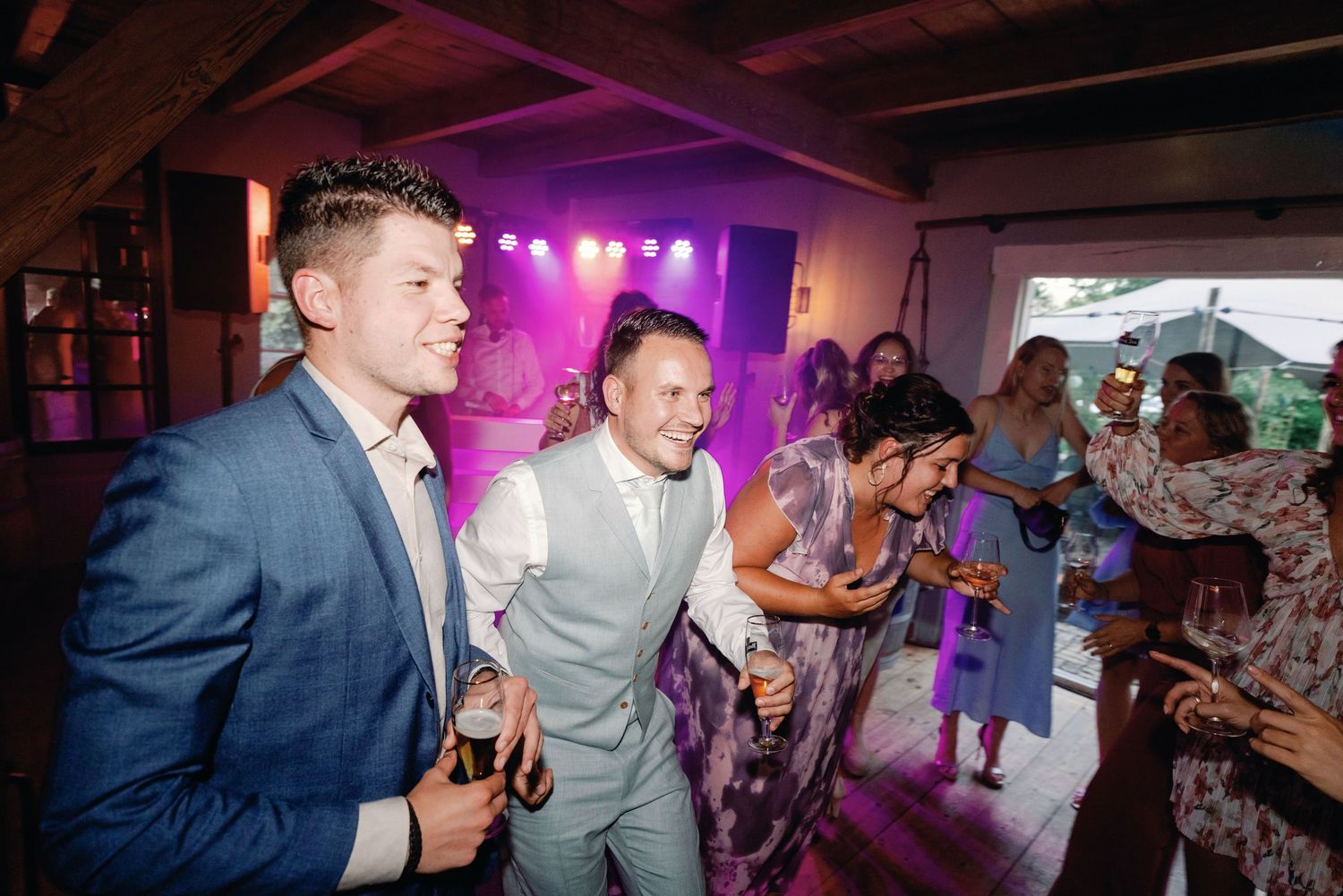 People dancing and celebrating at a lively wedding reception with purple lighting and festive atmosphere.