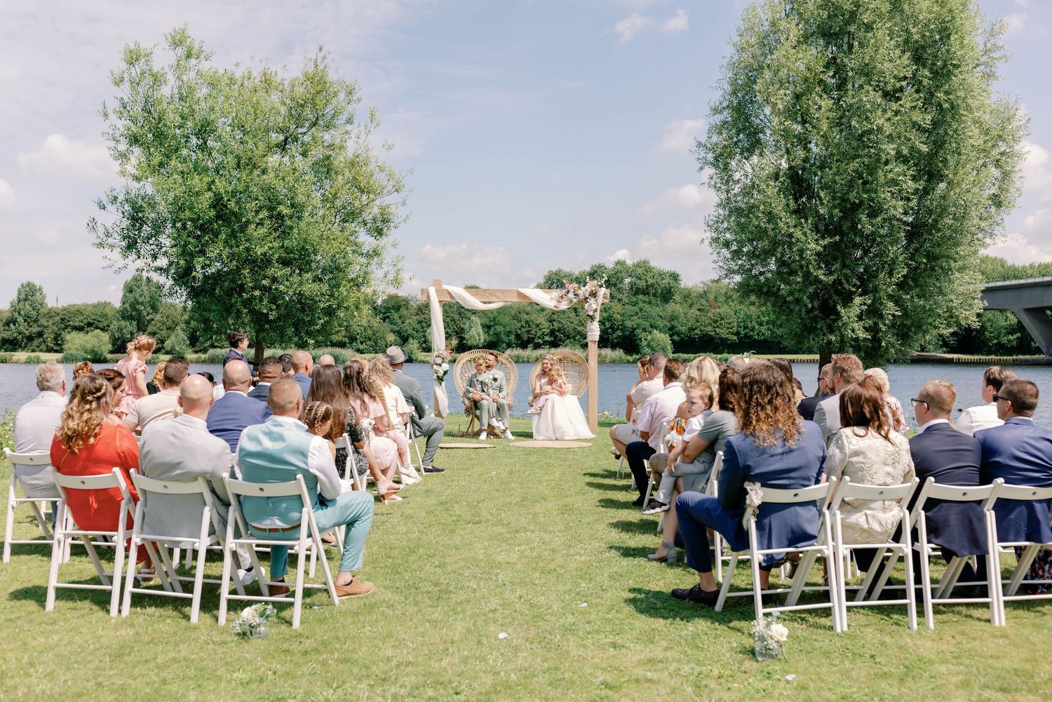 Panoramic view of guests seated in white chairs on a grassy lawn during an outdoor wedding ceremony.