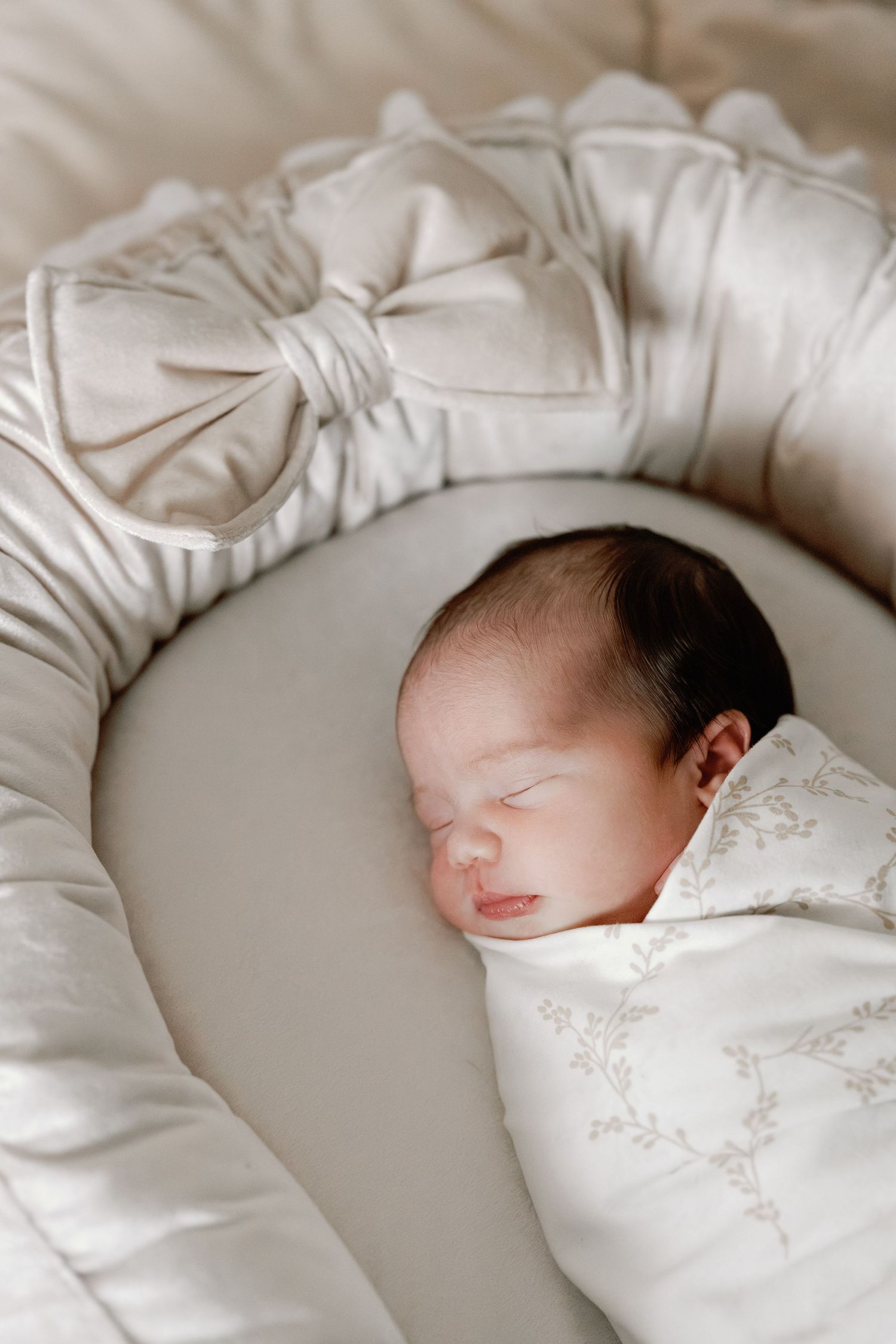 A sleeping newborn baby swaddled in white blankets rests peacefully on soft bedding.