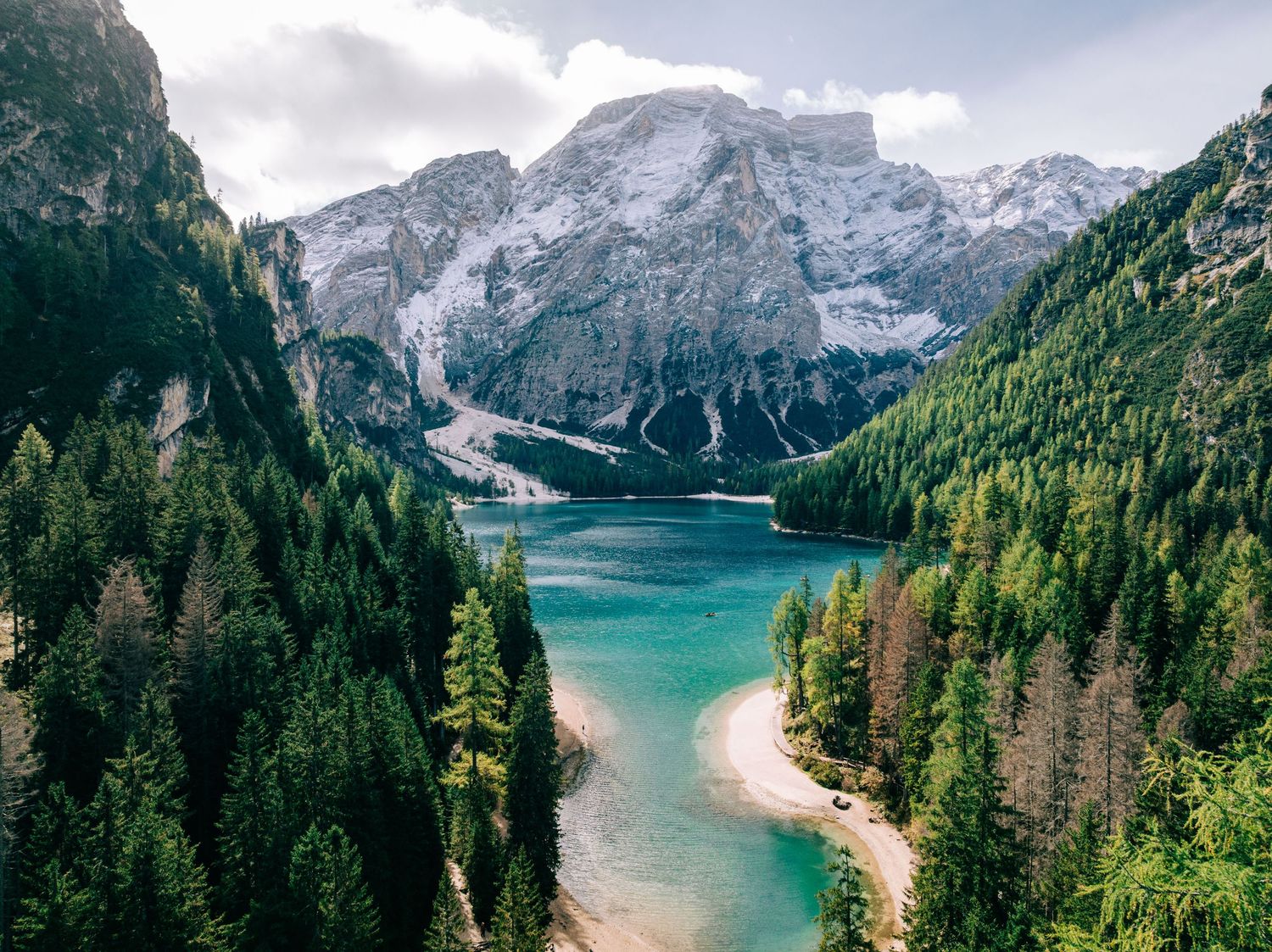 Panoramic view of a pristine alpine lake surrounded by evergreen forests and dramatic mountain peaks.
