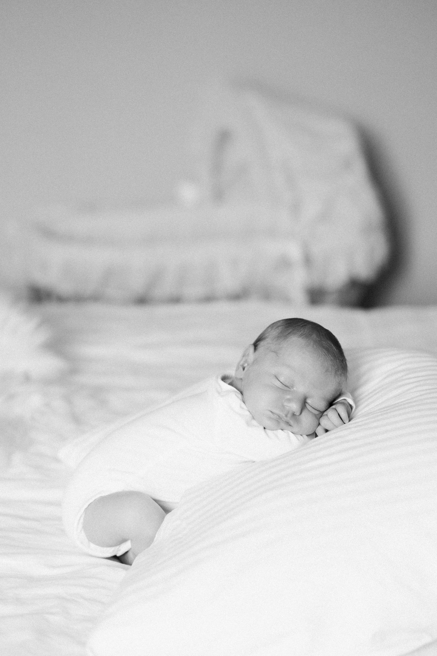 A peaceful black and white photograph of a sleeping newborn baby nestled in soft white bedding.