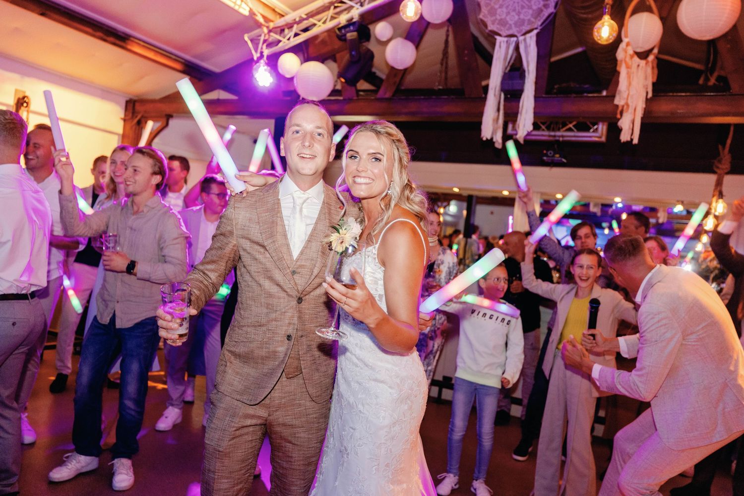 Wedding reception dance floor filled with guests celebrating under purple lighting and white paper lanterns.